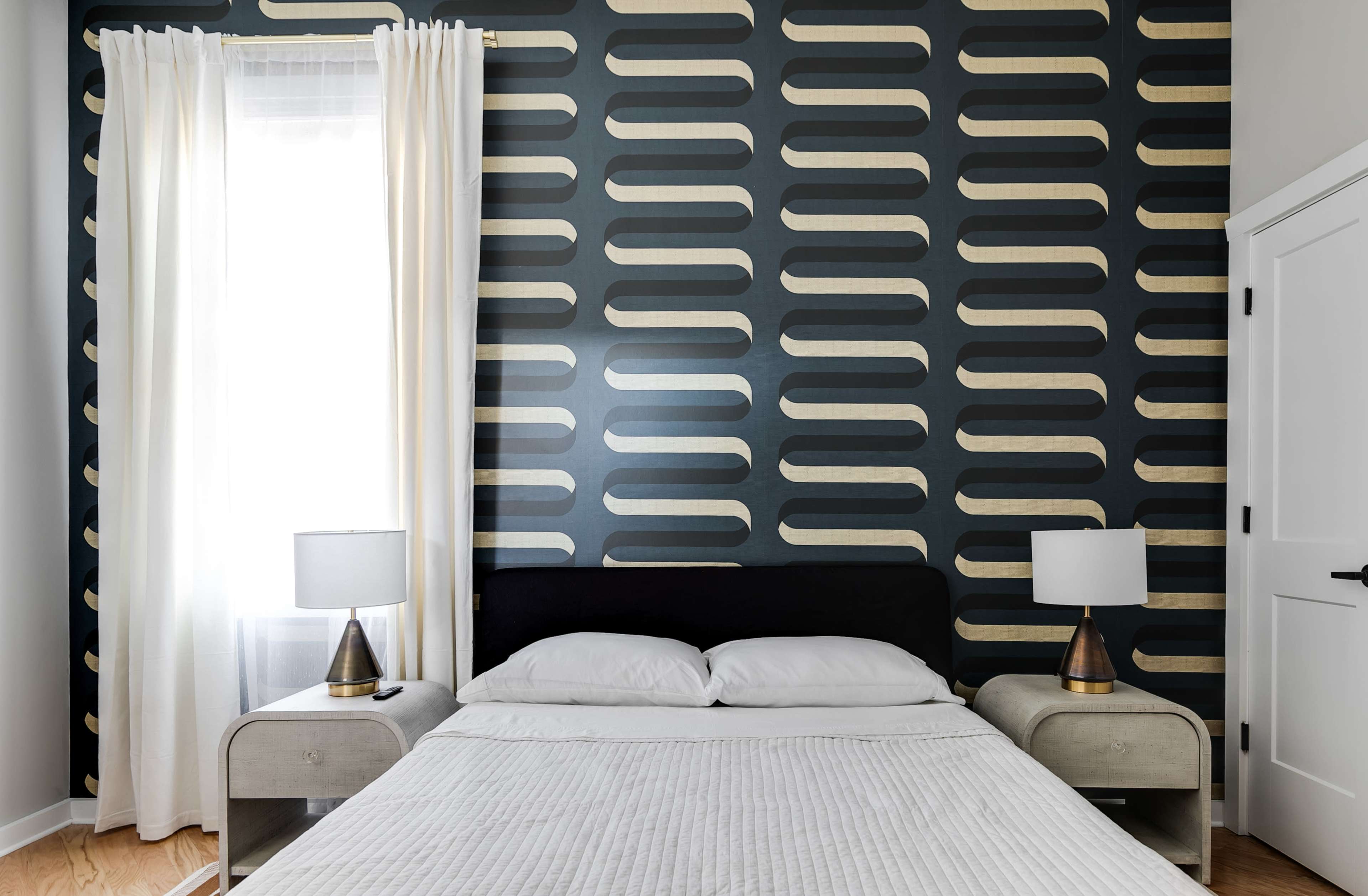 A bedroom with a patterned blue wall, a bed with white bedding, and two bedside tables with matching lamps.