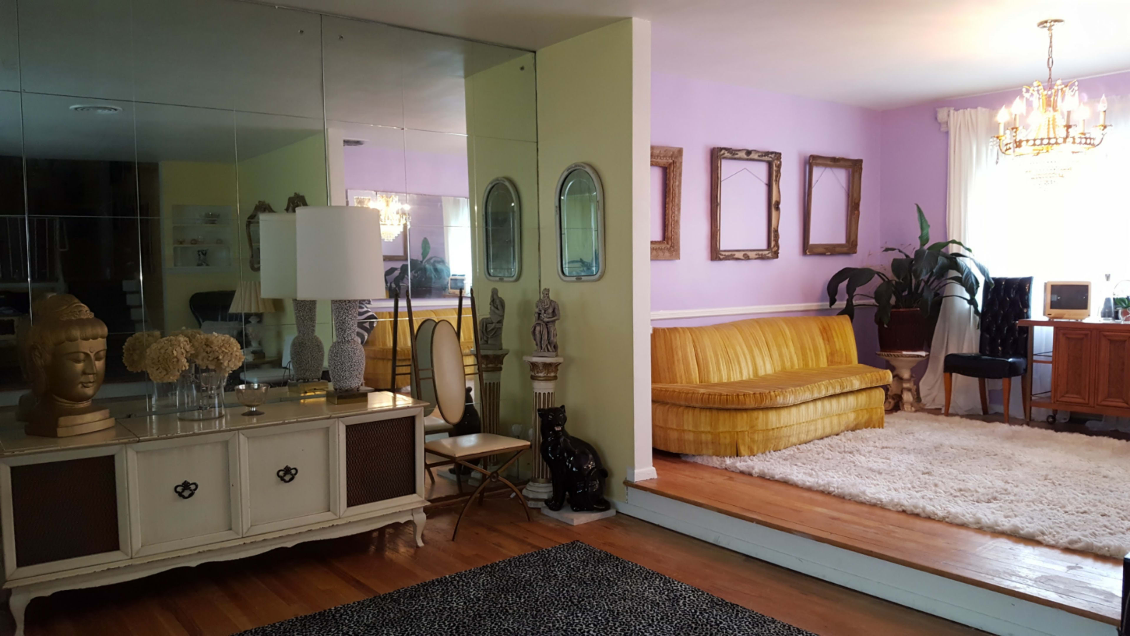 A bright living space featuring a mirrored wall, a yellow couch, decorative mirrors, and a stylish coffee table.