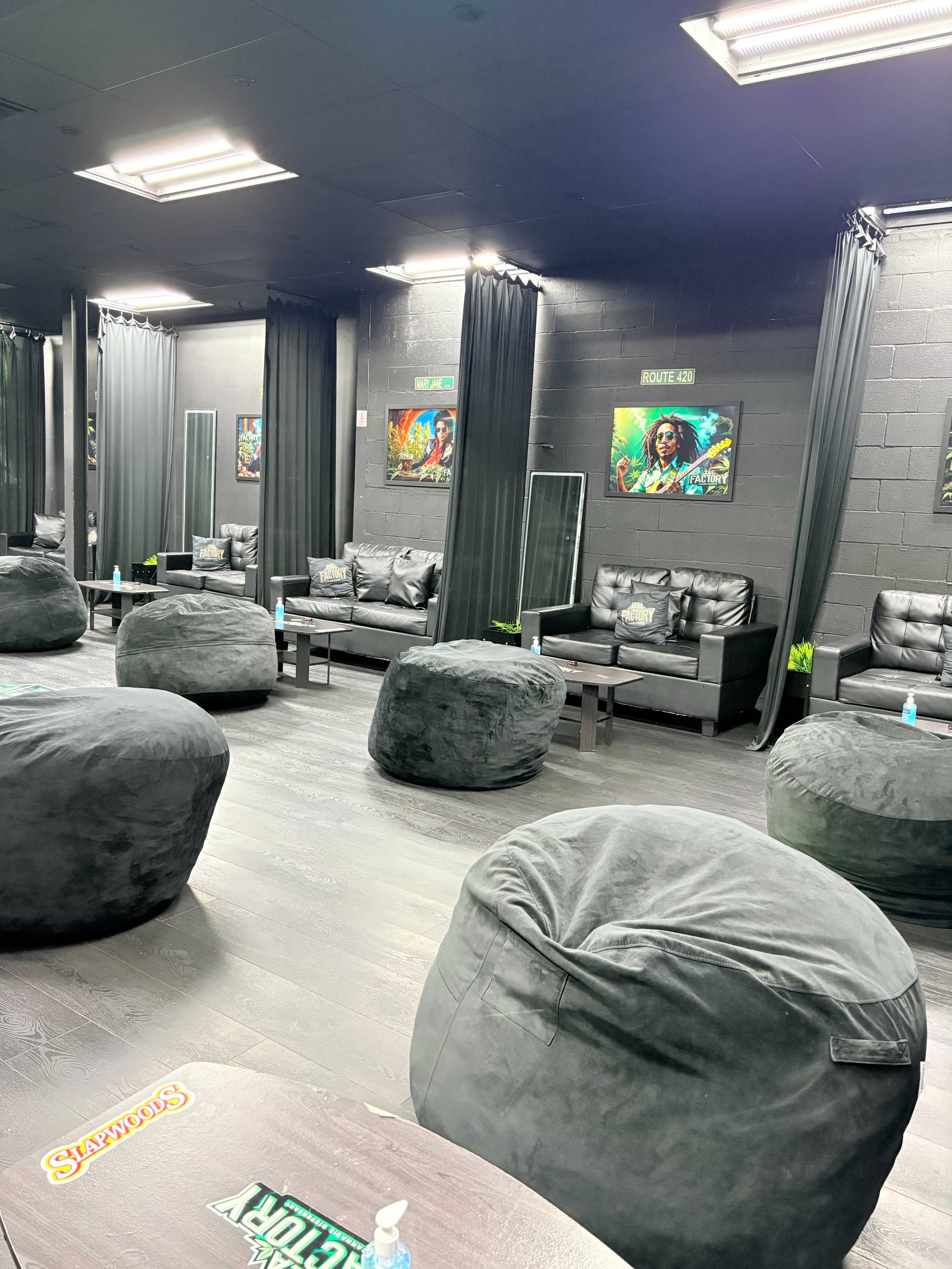 The image depicts a lounge area with several black bean bag chairs, dark couches, and framed artwork on the walls, all in a dimly lit space.