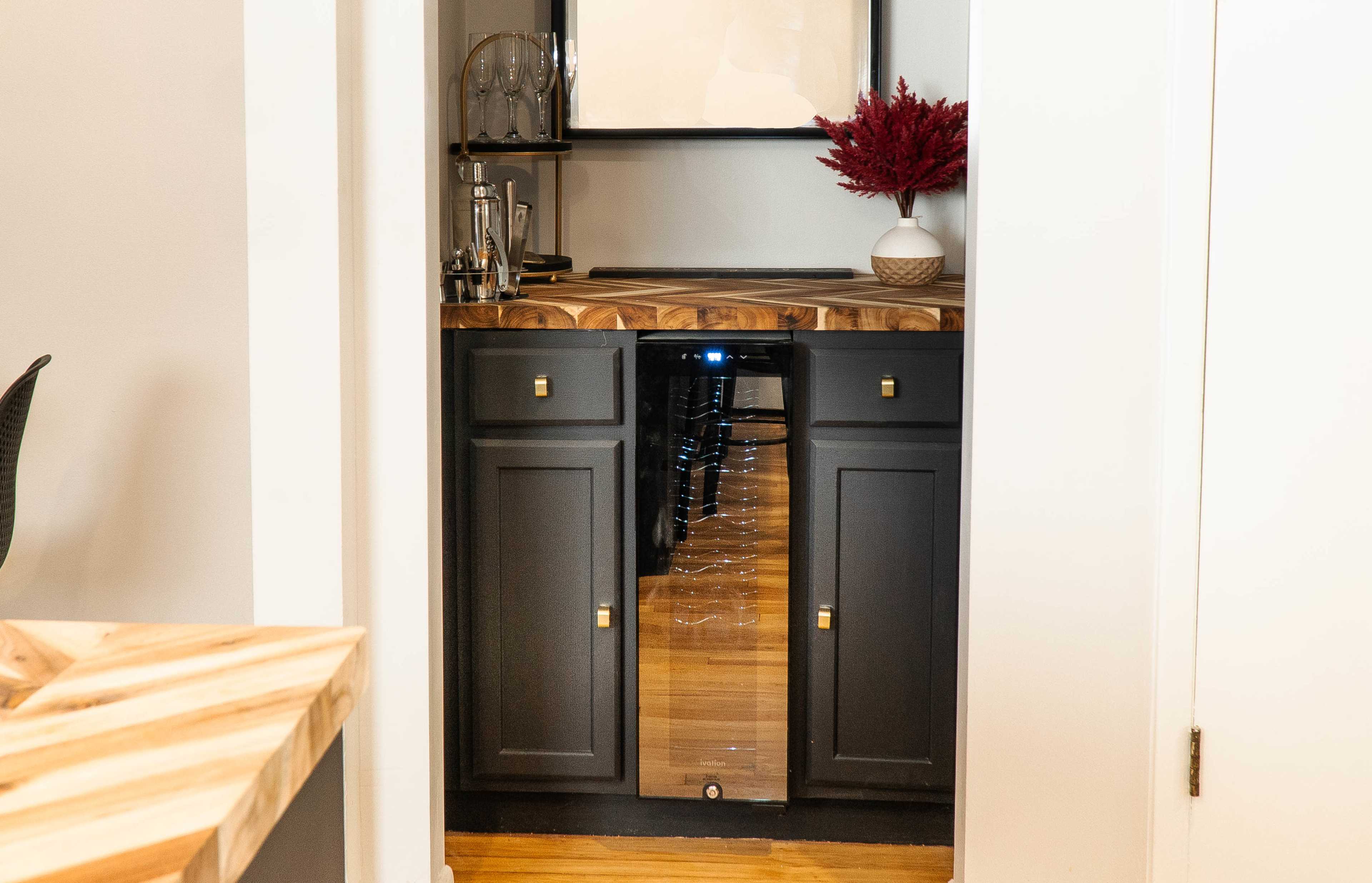 A small kitchen bar area with dark cabinetry, a wooden countertop, and a beverage cooler.