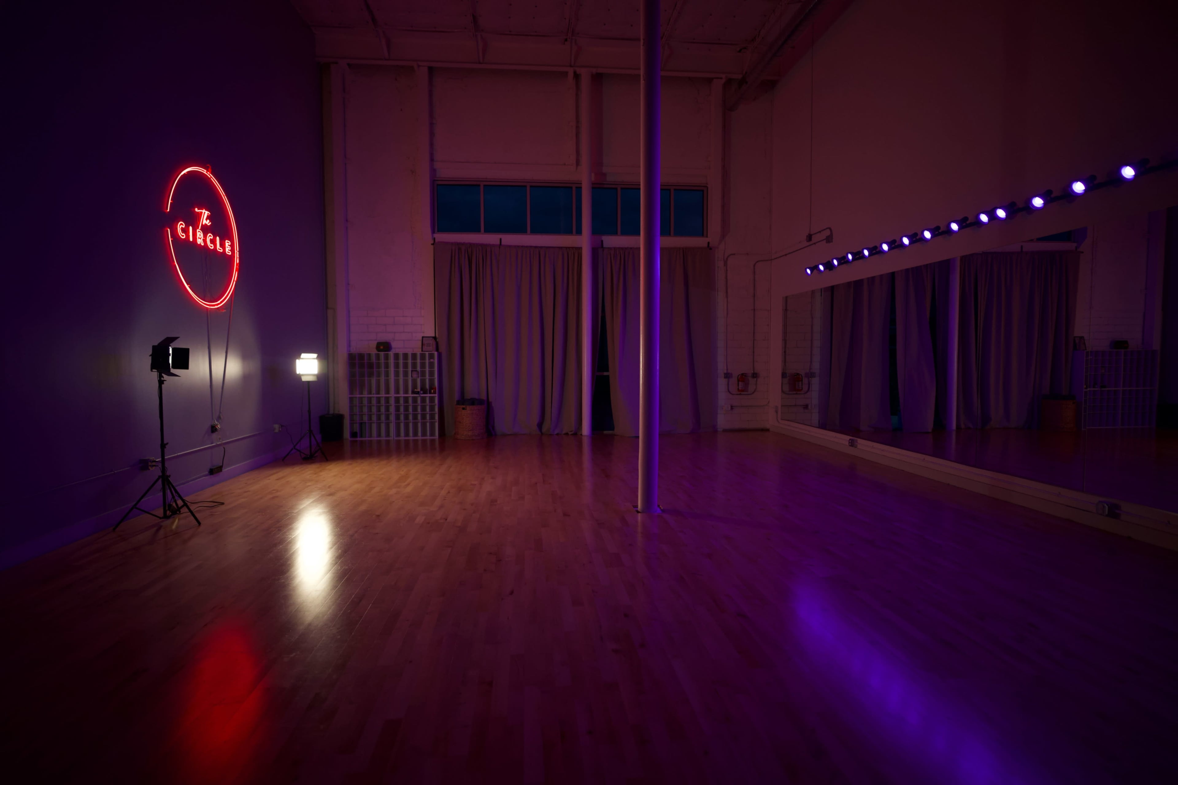 The image shows a dimly lit dance studio with hardwood floors, a large mirror, and a neon sign that reads "CIRCLE."