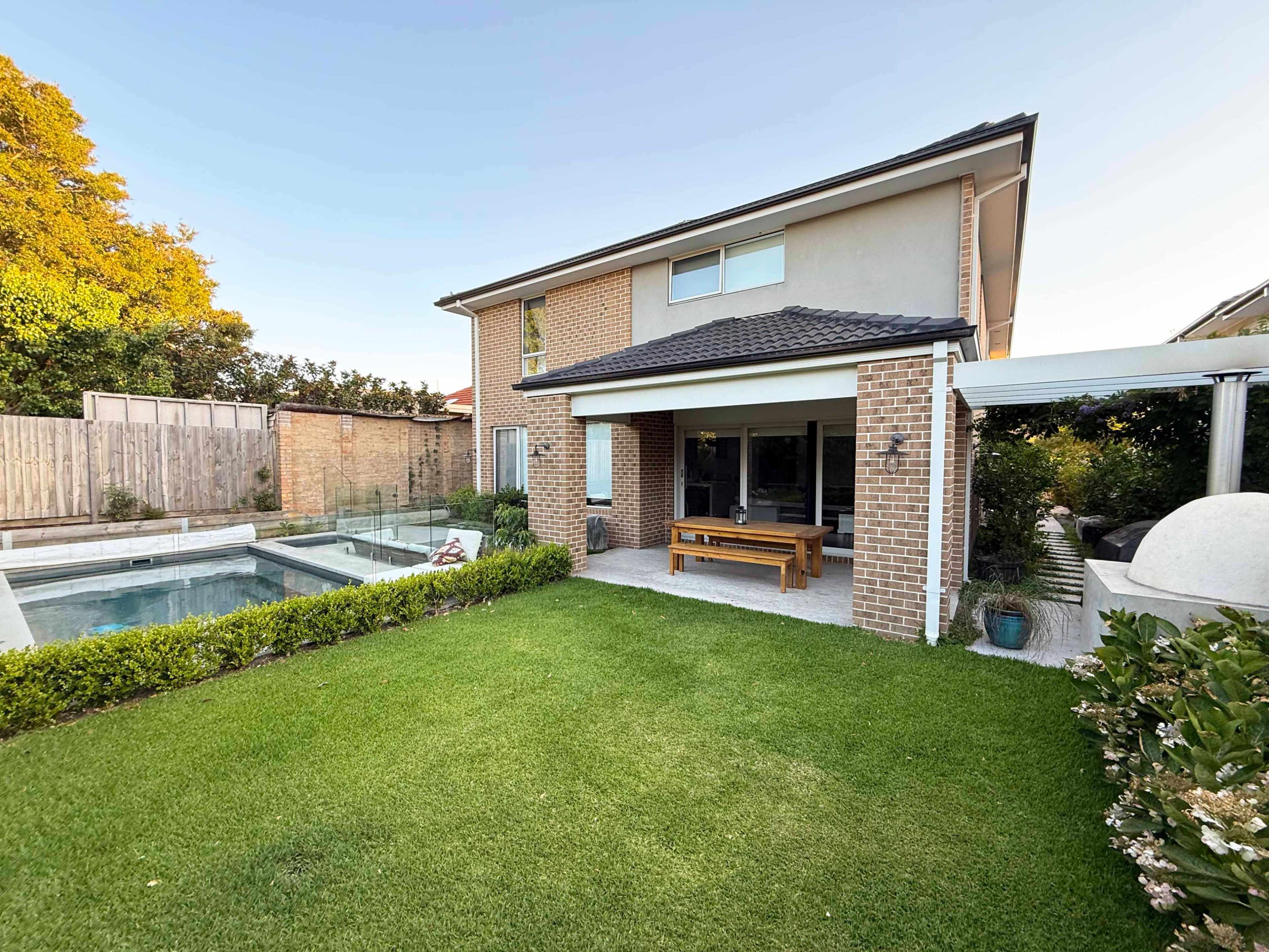 The image features a two-story house with a well-maintained garden and a swimming pool in the backyard.