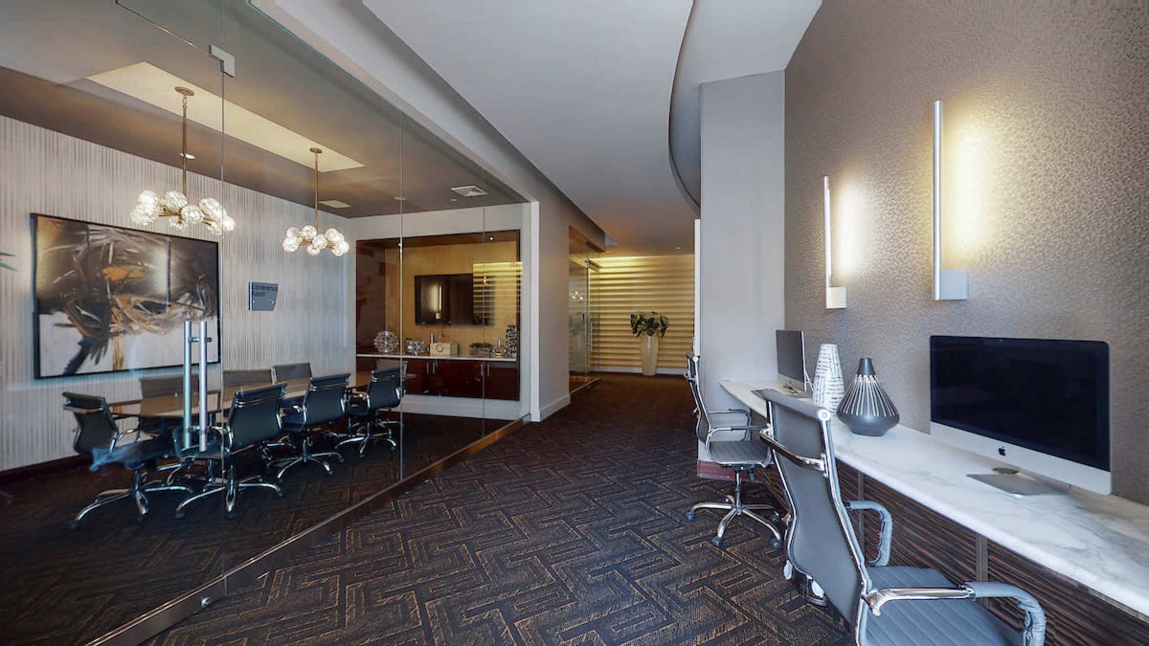 A modern office space featuring a glass-walled conference room, a reception area with a large painting, and workstations with computers along a marble counter.