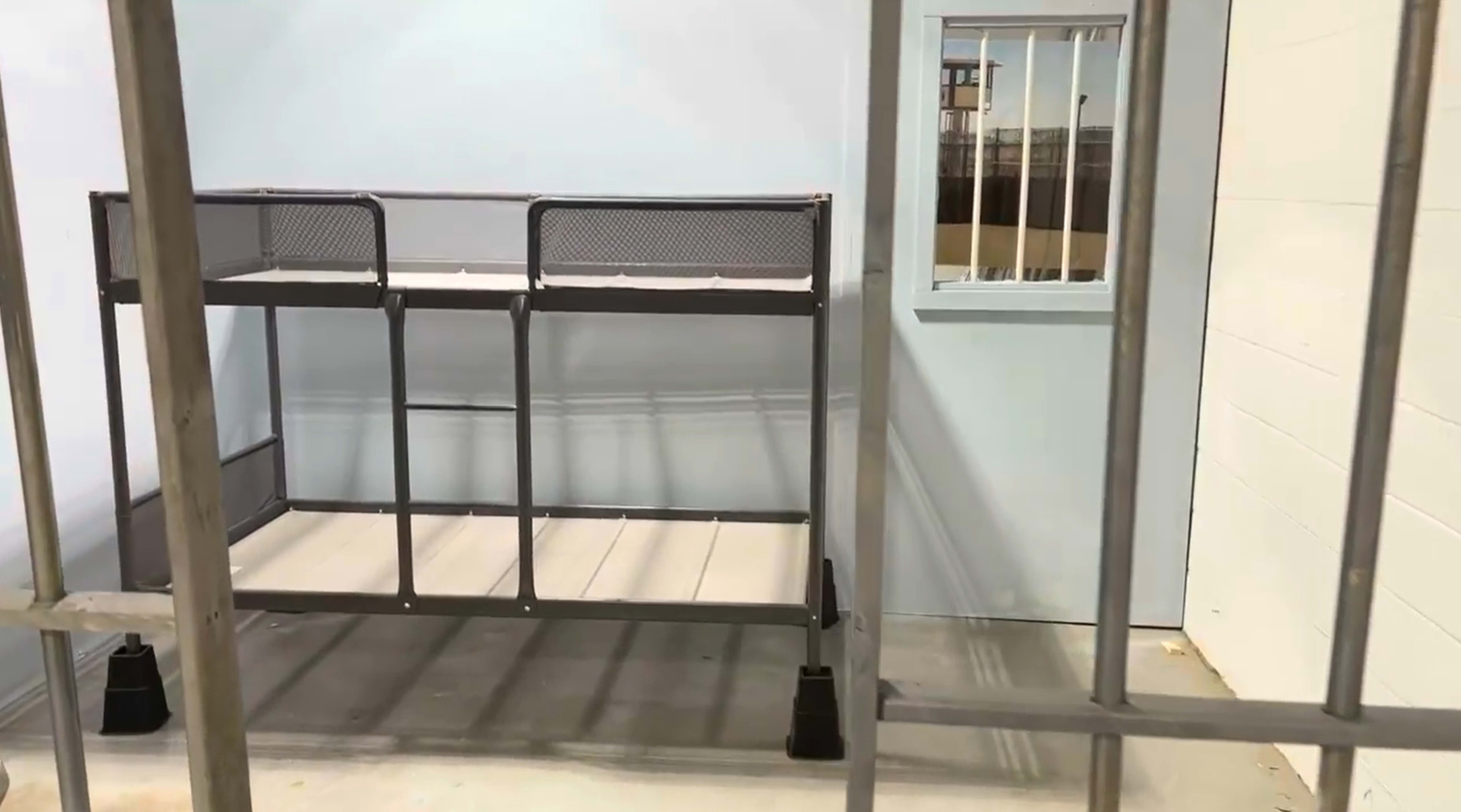 The image shows a partially constructed room with a metal frame and a shelving unit against a light blue wall, featuring a barred window.