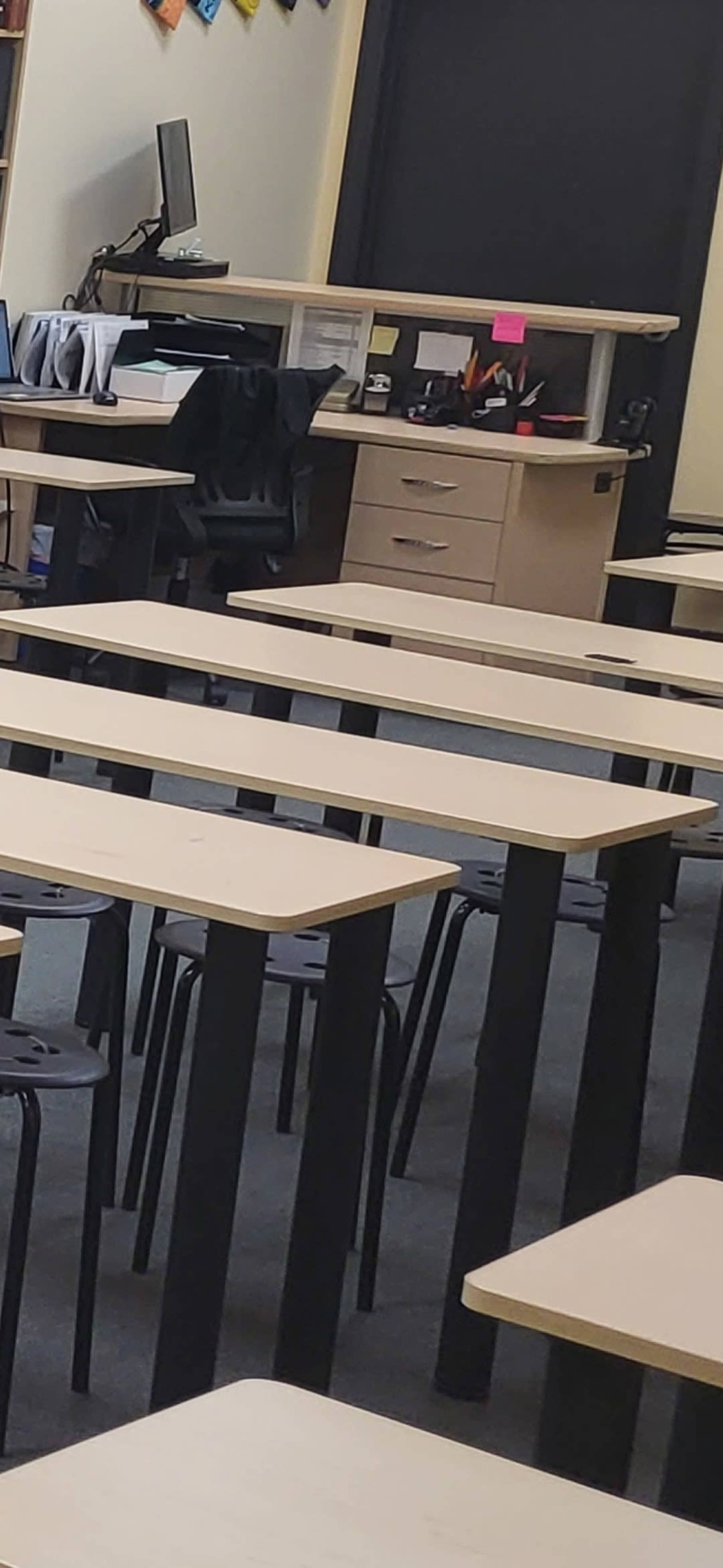 A classroom with several rows of minimalist tables and a desk at the front.