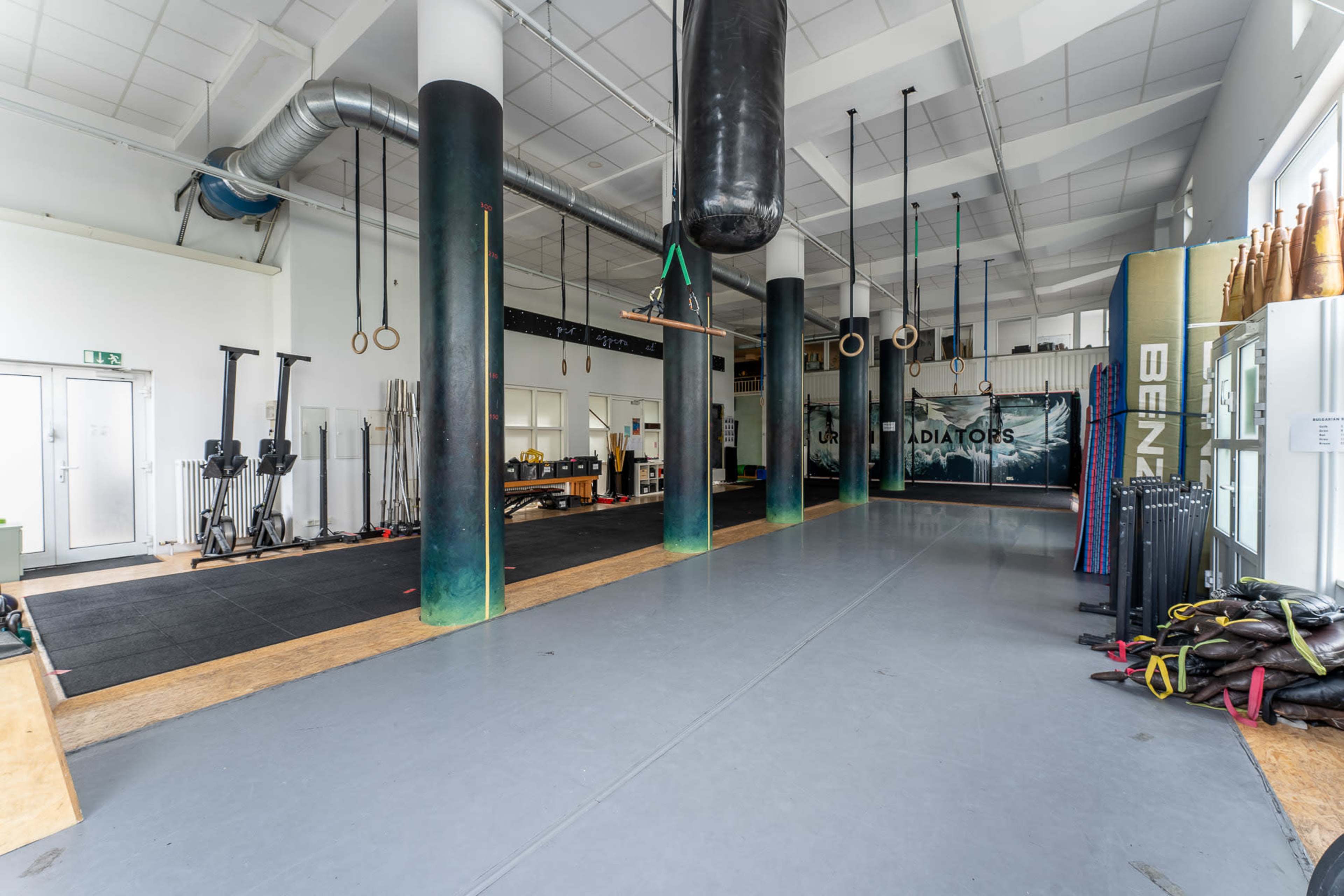 A spacious gym interior featuring various gym equipment, suspended rings, and a heavy bag, with a clean, organized layout.