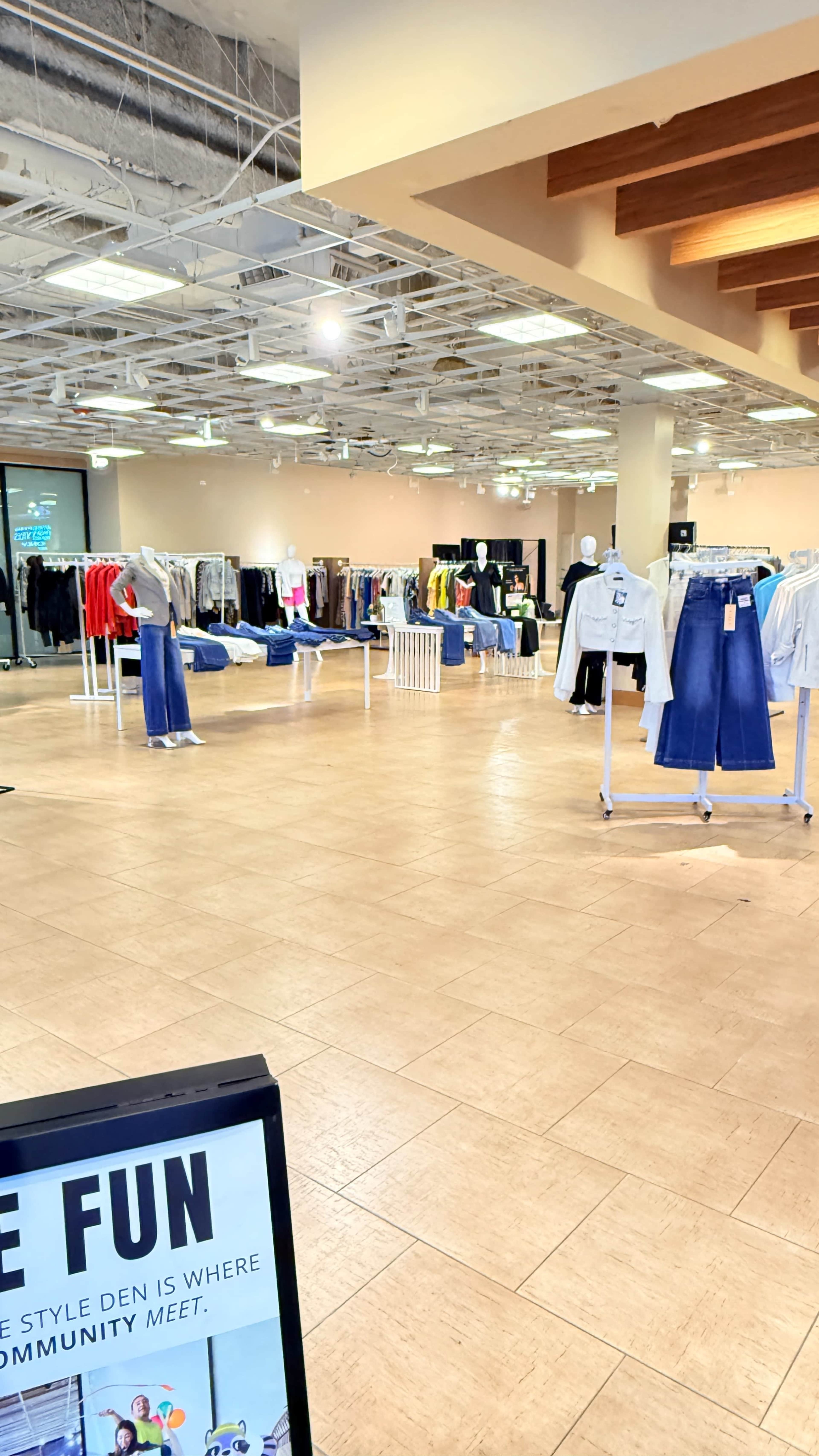 The image shows a spacious clothing store with racks of various apparel neatly arranged in a well-lit interior.