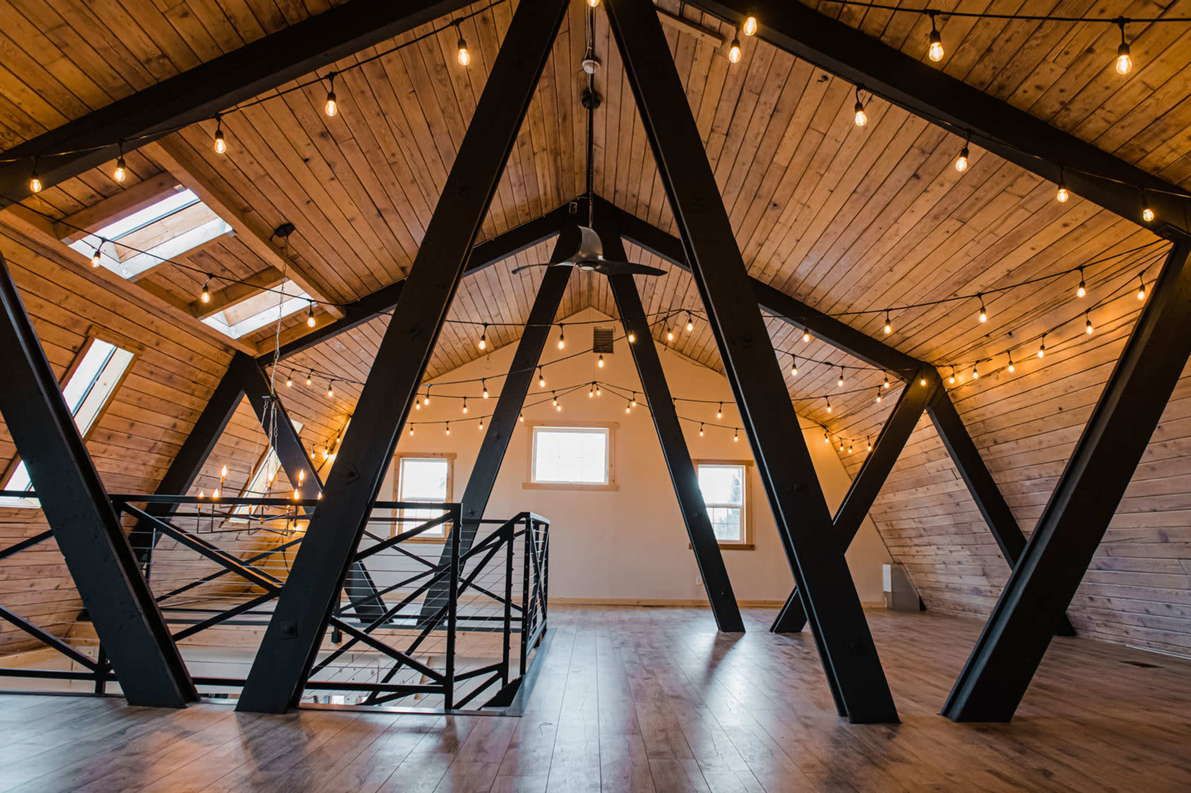 An interior space with wooden beams and string lights, featuring a spacious, open layout with large windows.