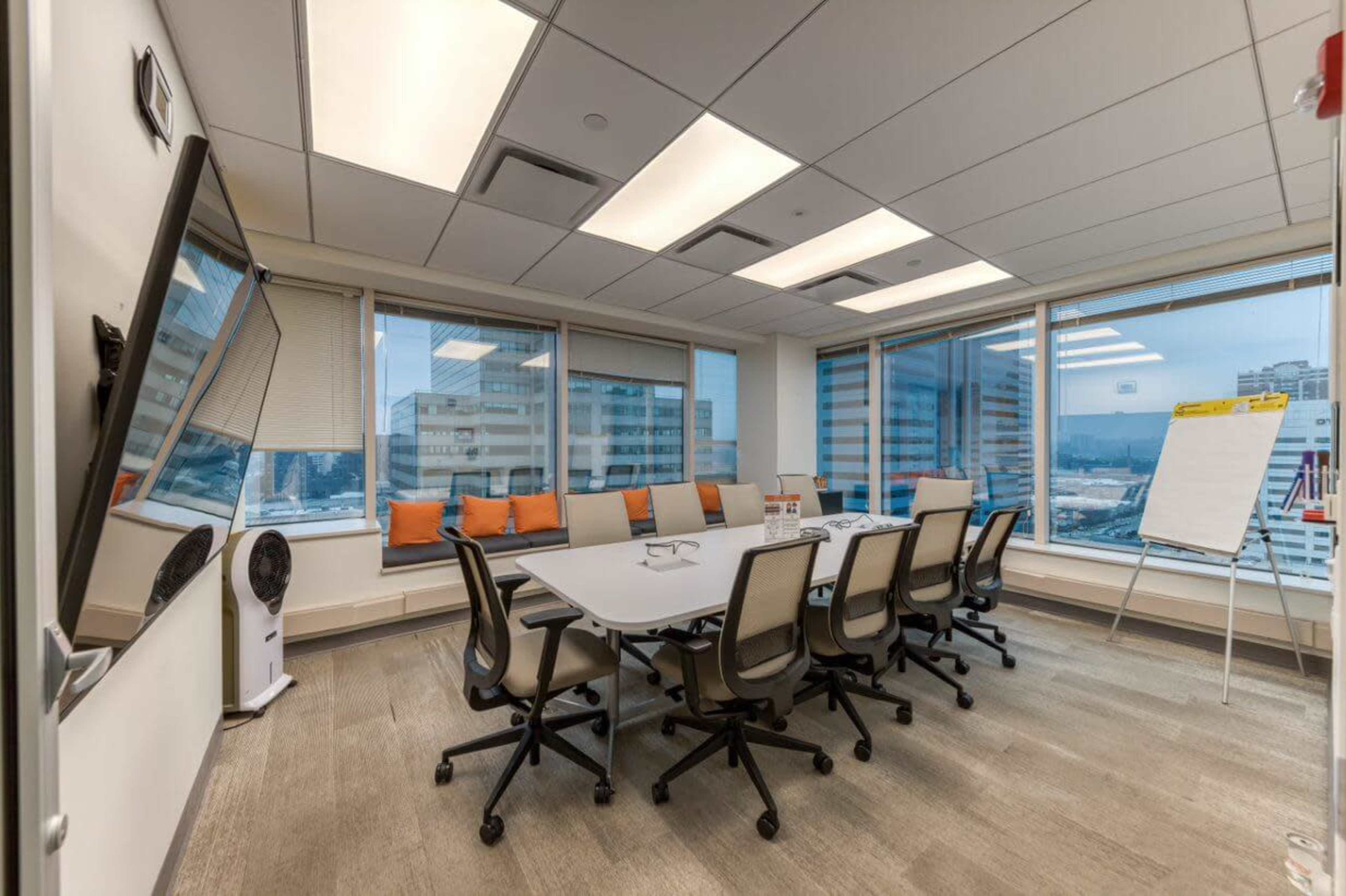 A conference room featuring a long table surrounded by chairs, a whiteboard, and large windows offering a view of the city.