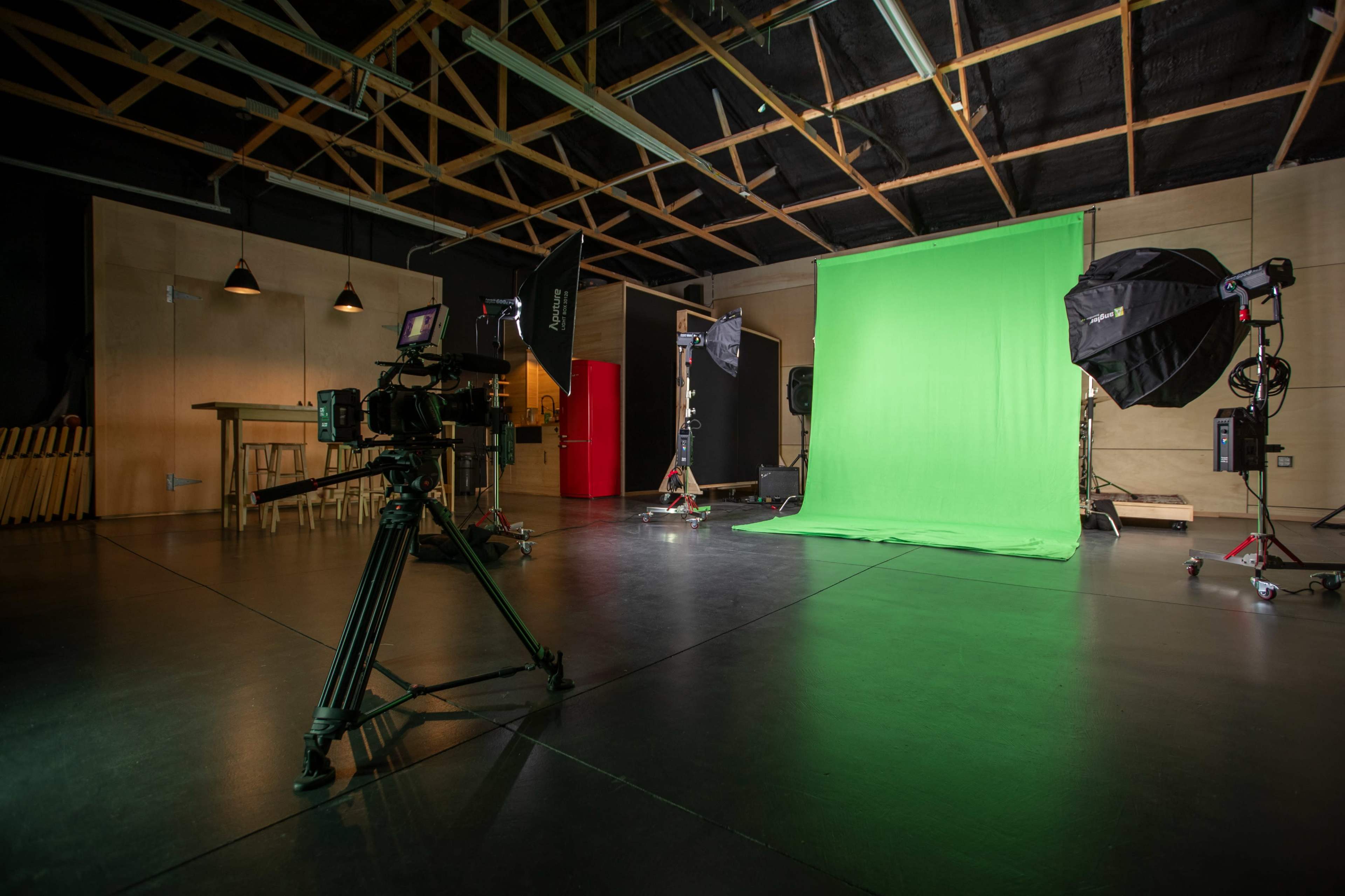 The image shows a photography studio equipped with a green screen, lighting equipment, and a camera setup on a tripod.