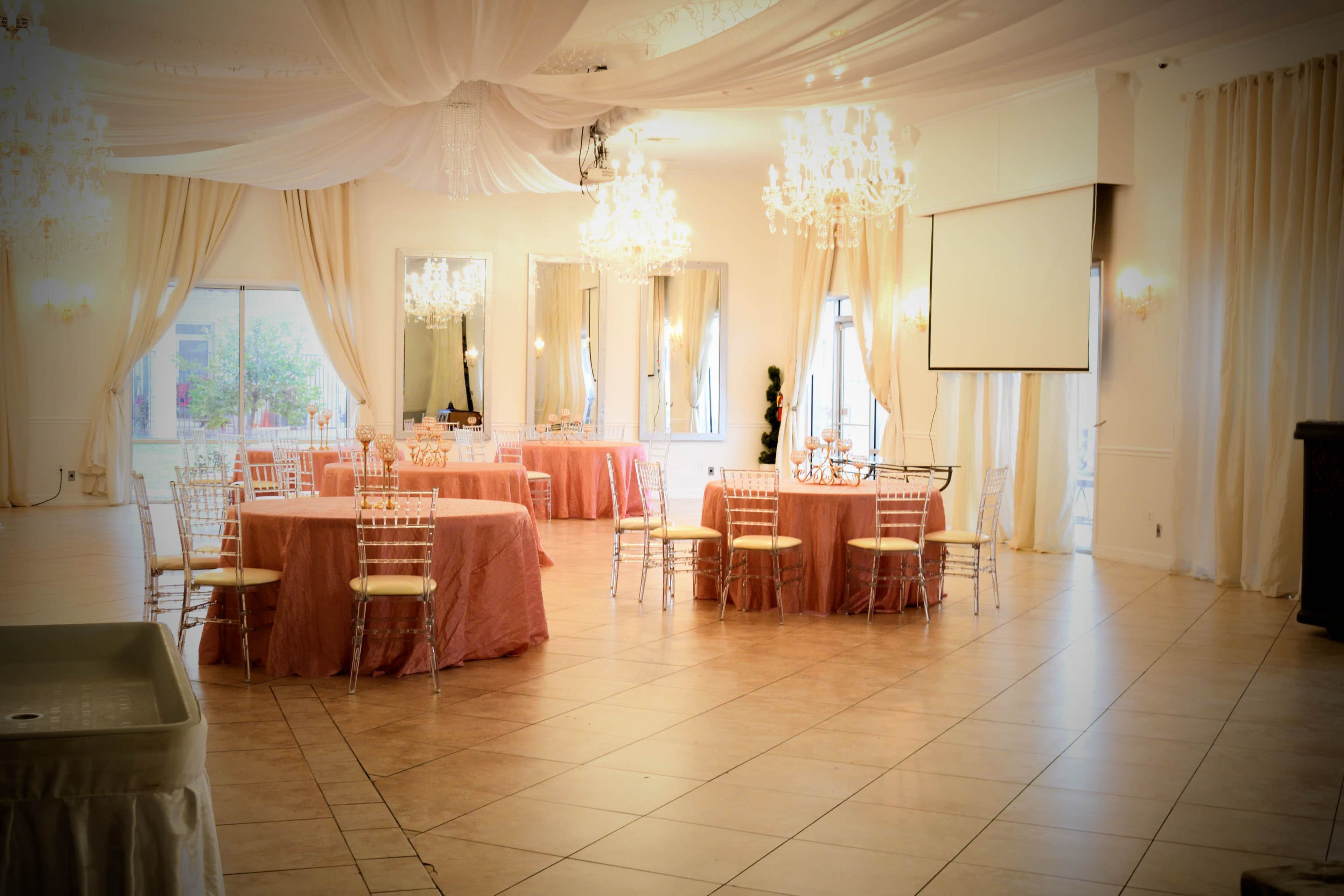 A banquet hall set up with round tables covered in pink tablecloths and adorned with elegant chandeliers hanging from the ceiling.