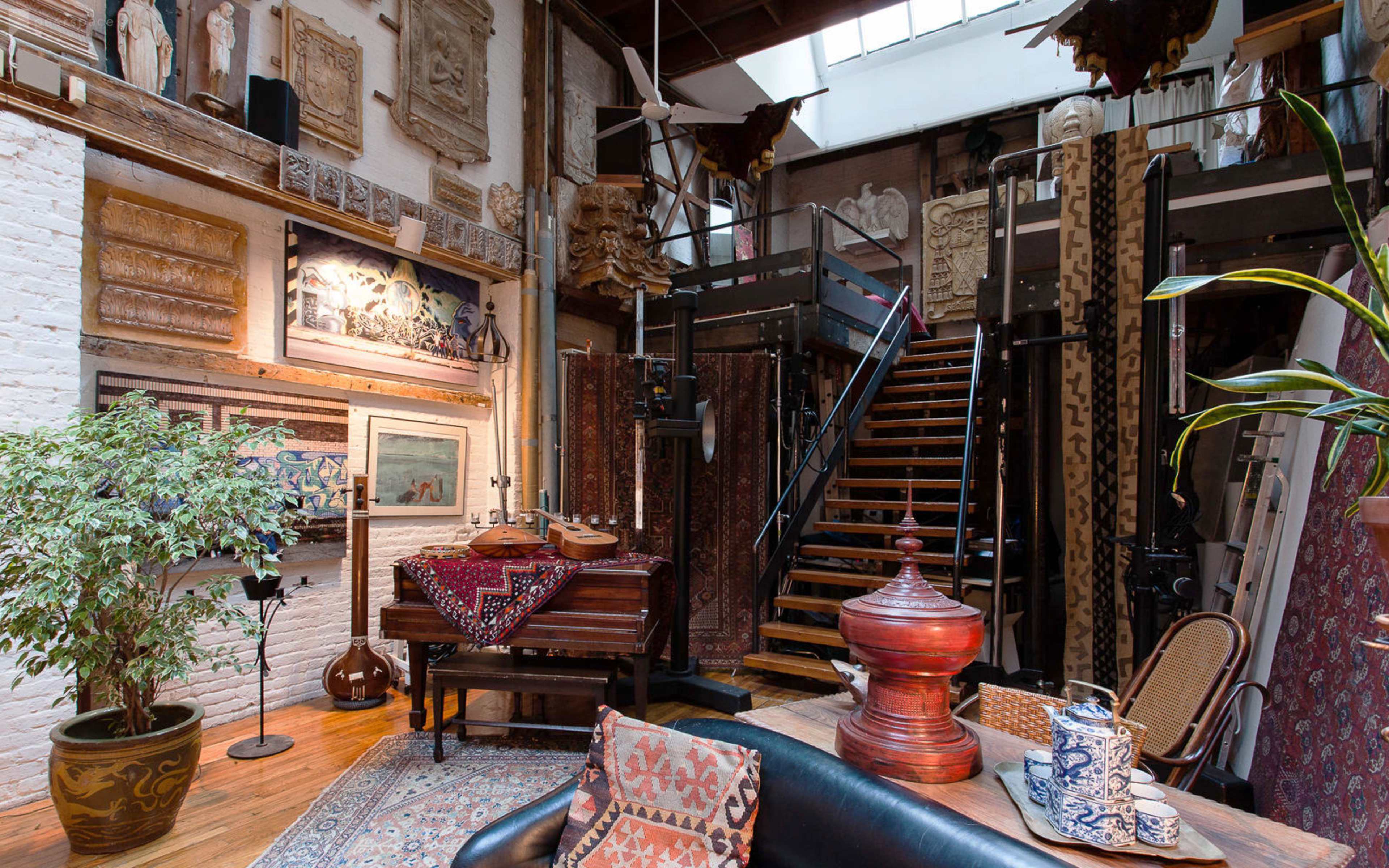 A spacious interior featuring a staircase, various artworks on the walls, a grand piano, and ornate decorative elements throughout.