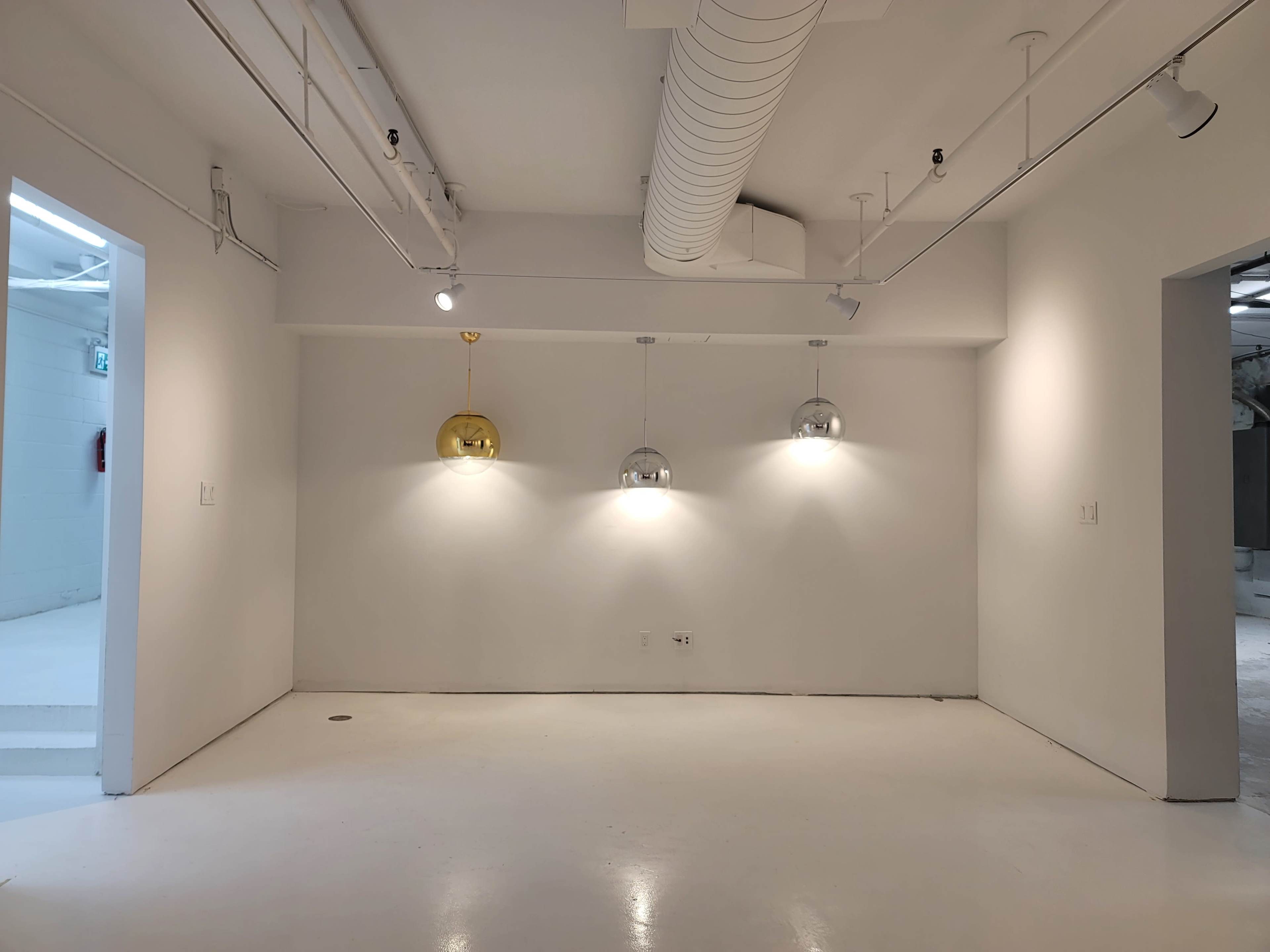 A minimalist white room with three pendant lights hanging from the ceiling and a doorway on the left side.