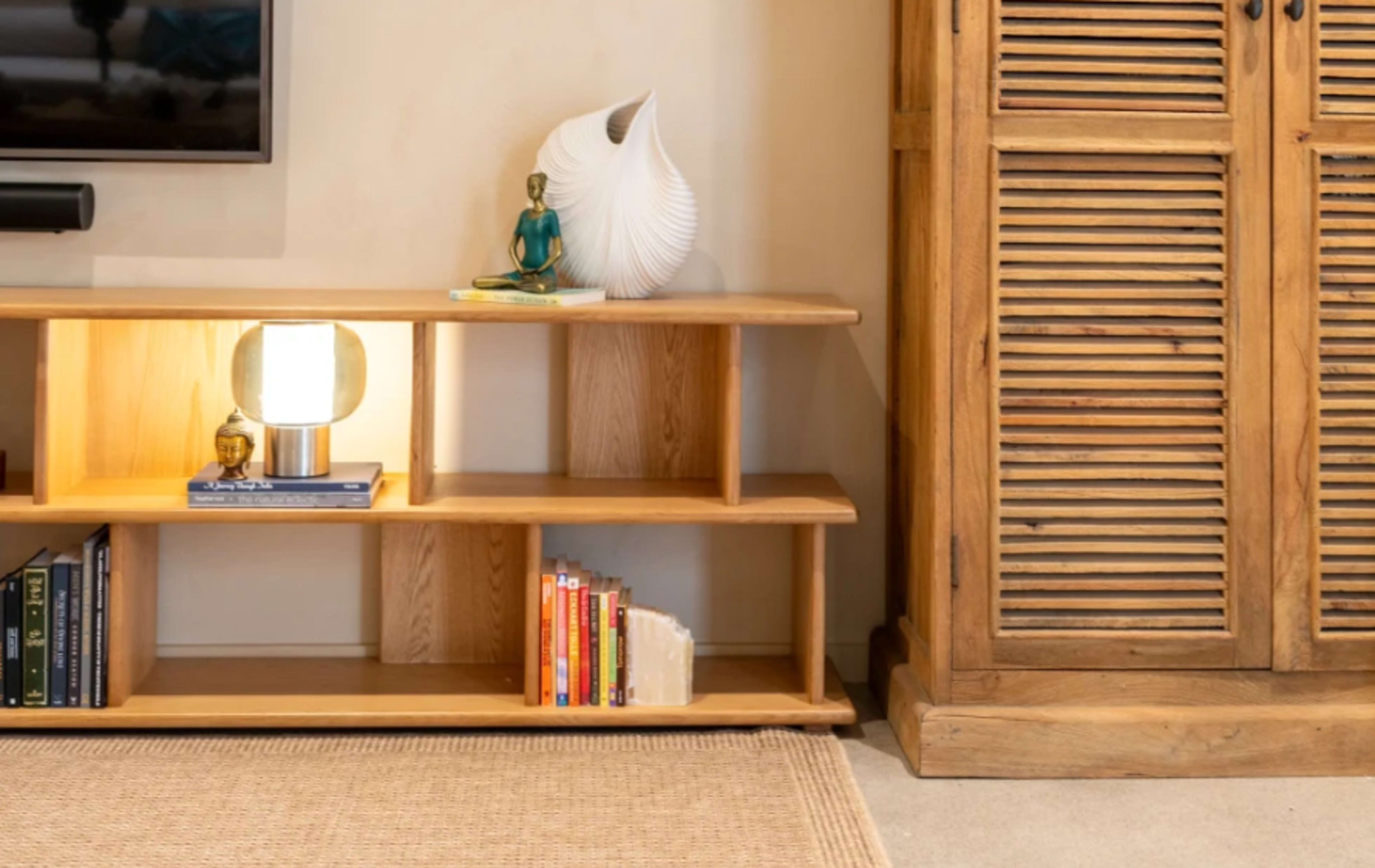 The image shows a wooden shelf with a lamp, books, and a decorative figure, adjacent to a wooden cabinet with louvered doors.