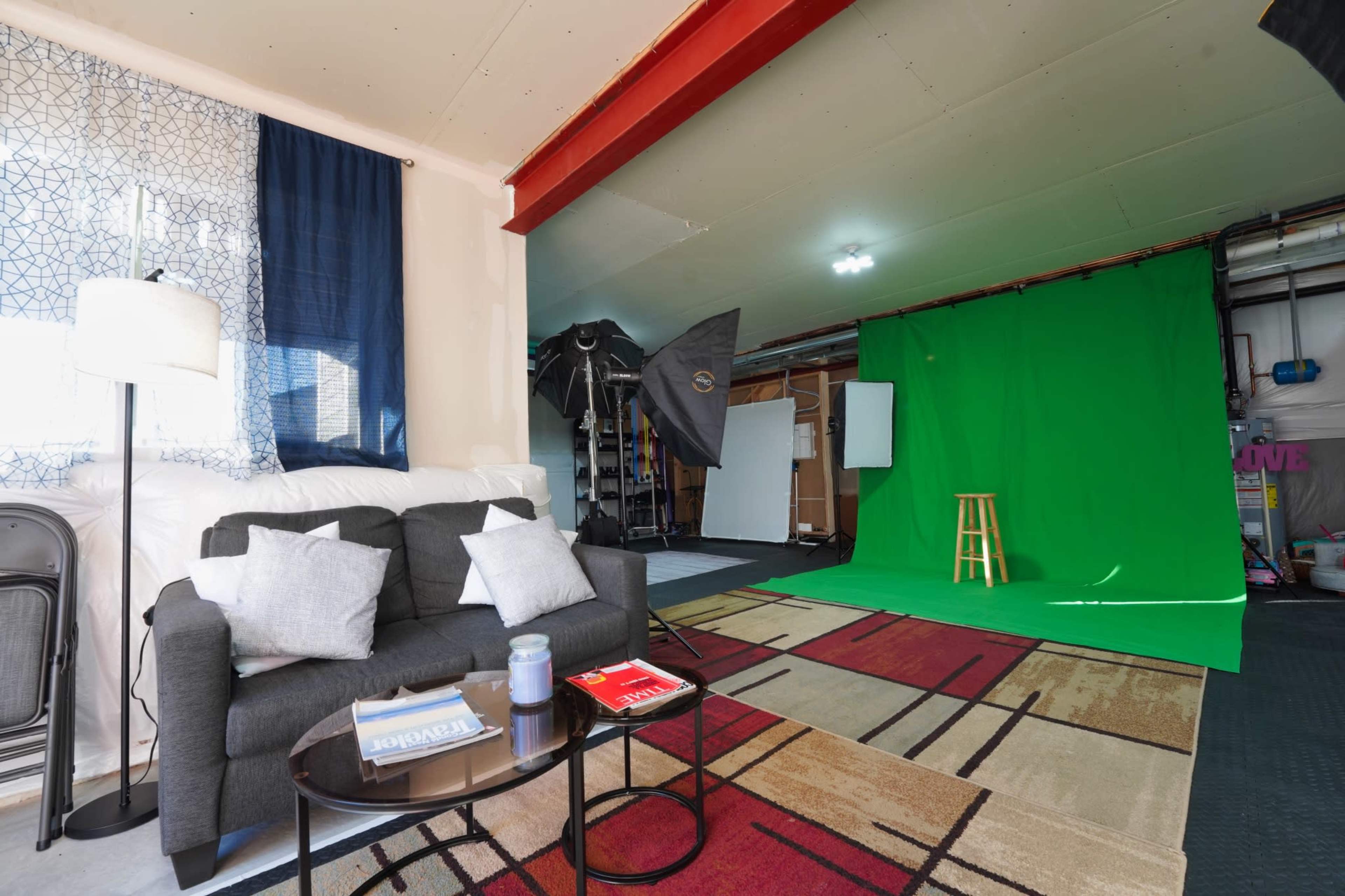 The image shows a studio space that features a green screen setup, photography equipment, a couch, and various props.