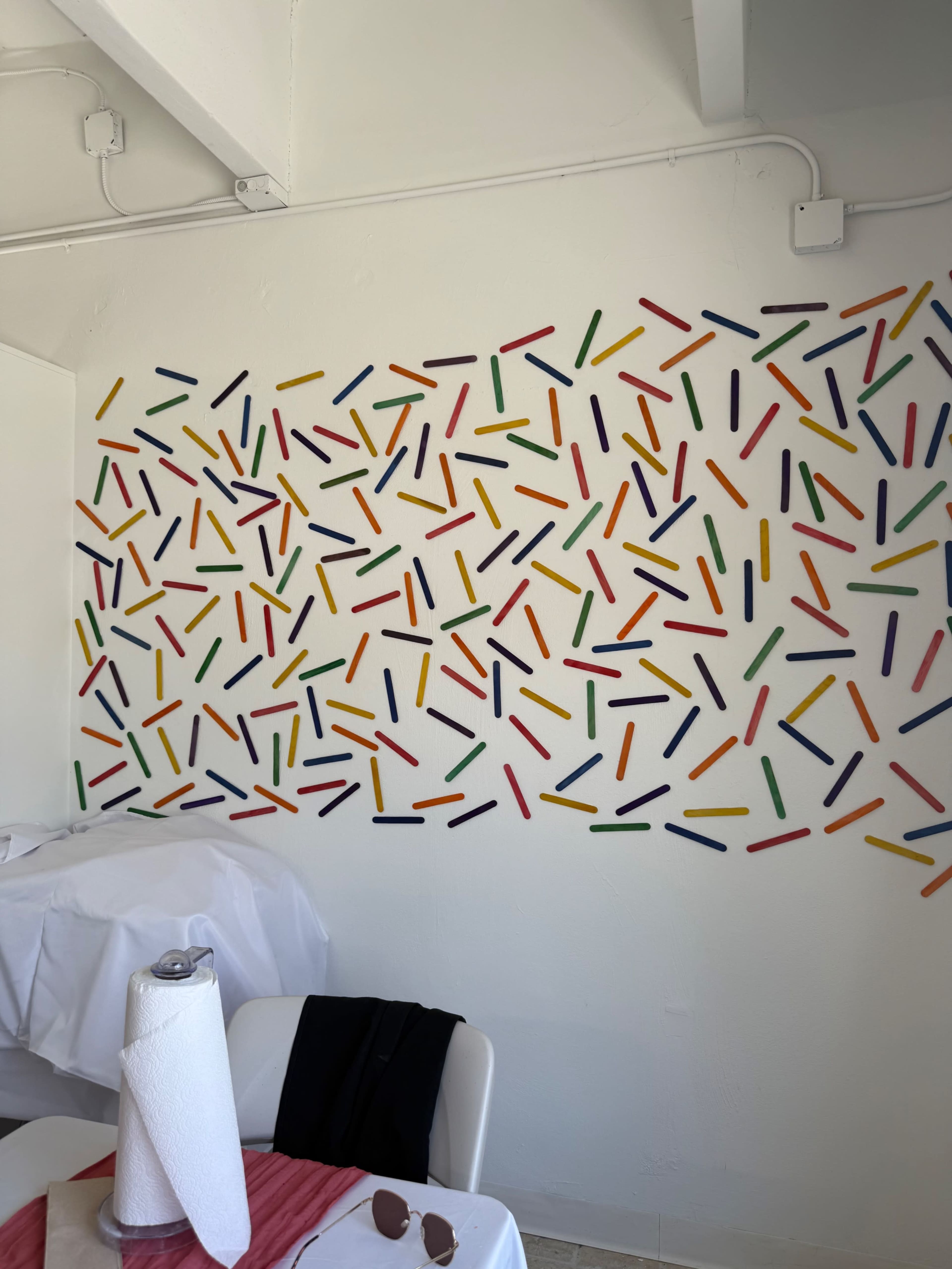 The image shows a white wall decorated with colorful, stick-like shapes arranged in a random pattern.