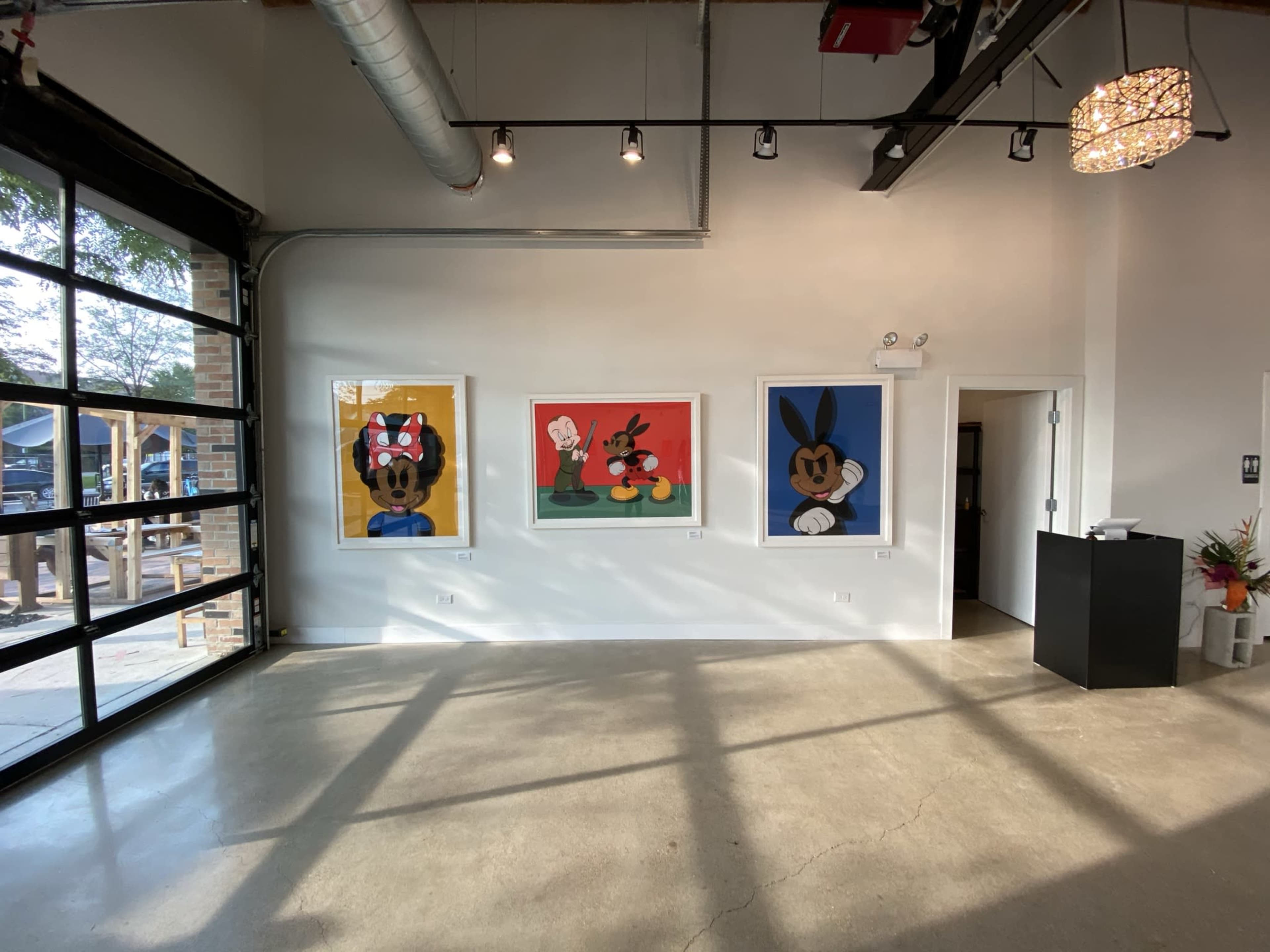 A modern interior space featuring three large framed artworks of cartoon characters on a white wall, with a reception desk and an open door visible.