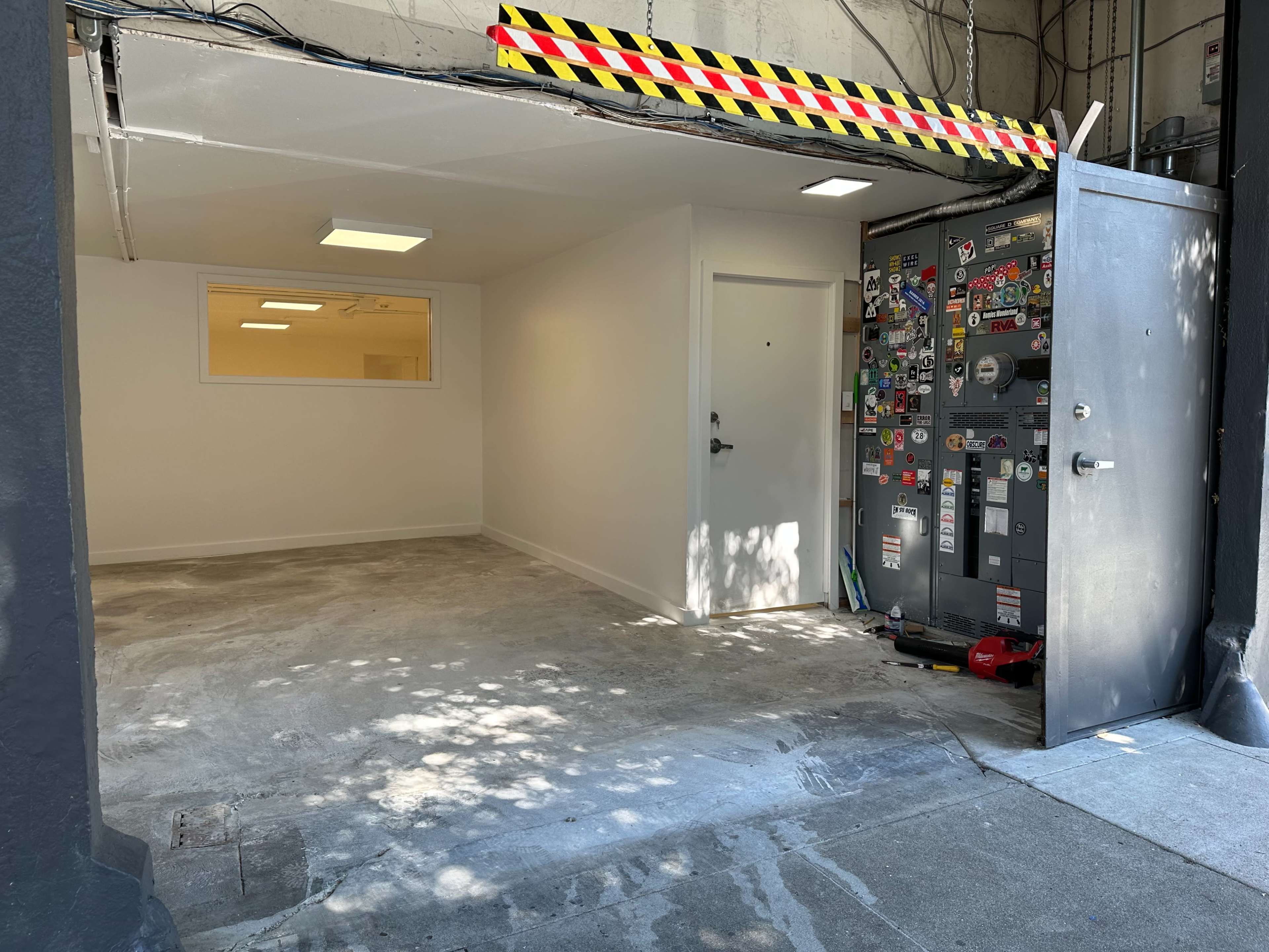 An empty garage with a white wall and a door, featuring a utility panel covered in various stickers next to it.