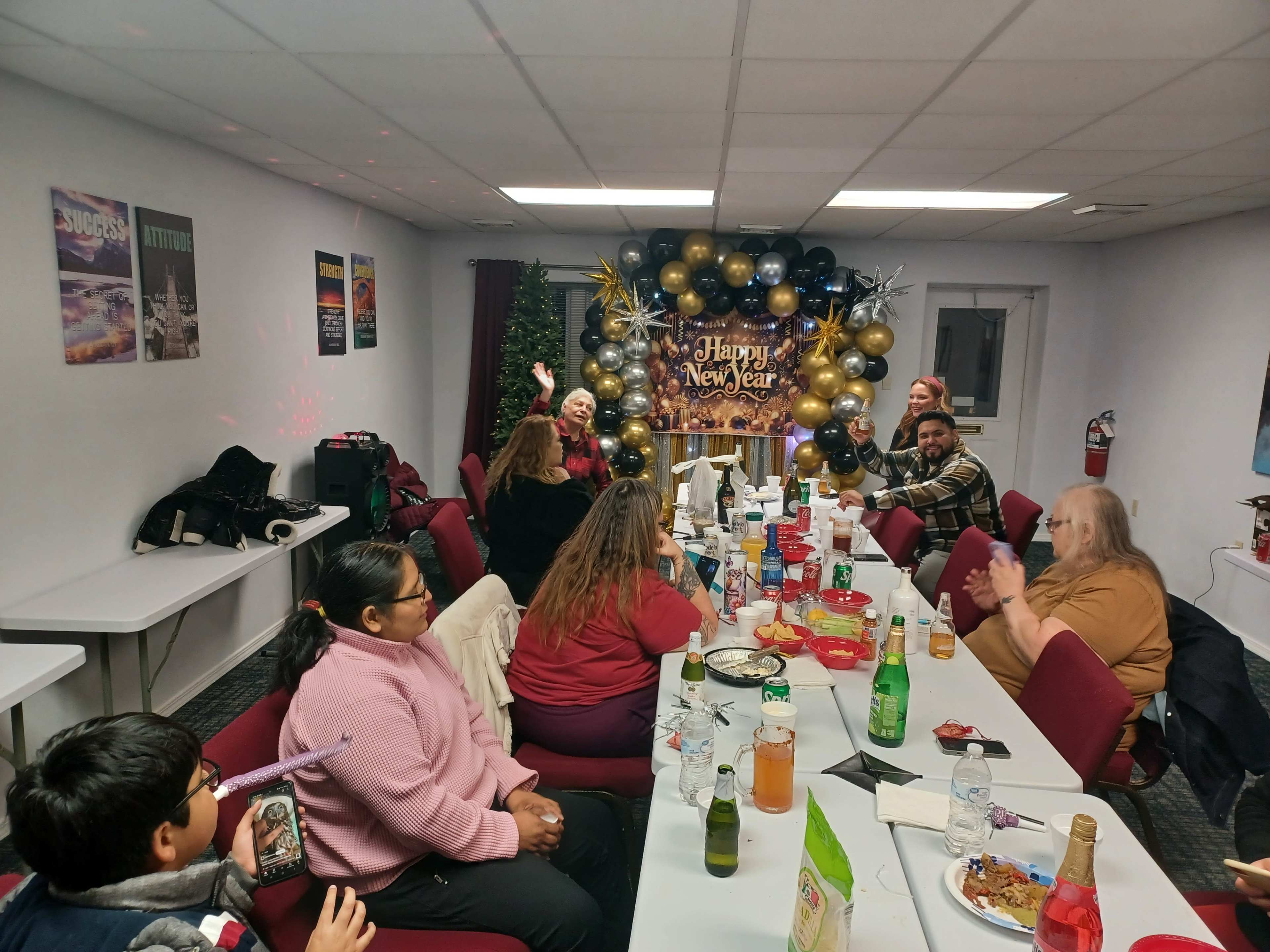 A group of people is celebrating a New Year’s gathering in a decorated room with balloons and a festive backdrop.
