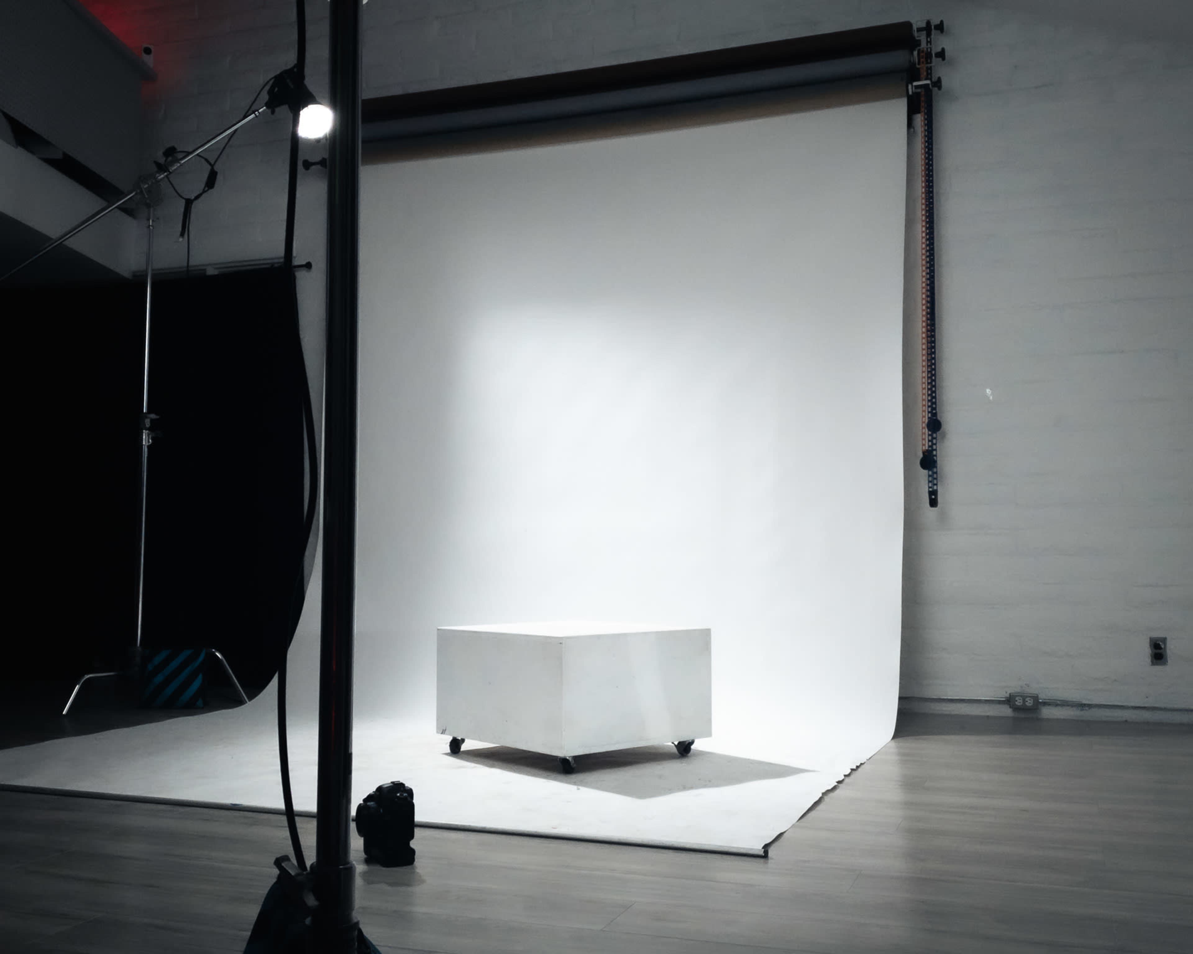 A white studio backdrop is set up with a small white box on wheels in the center of the room, surrounded by lighting equipment.