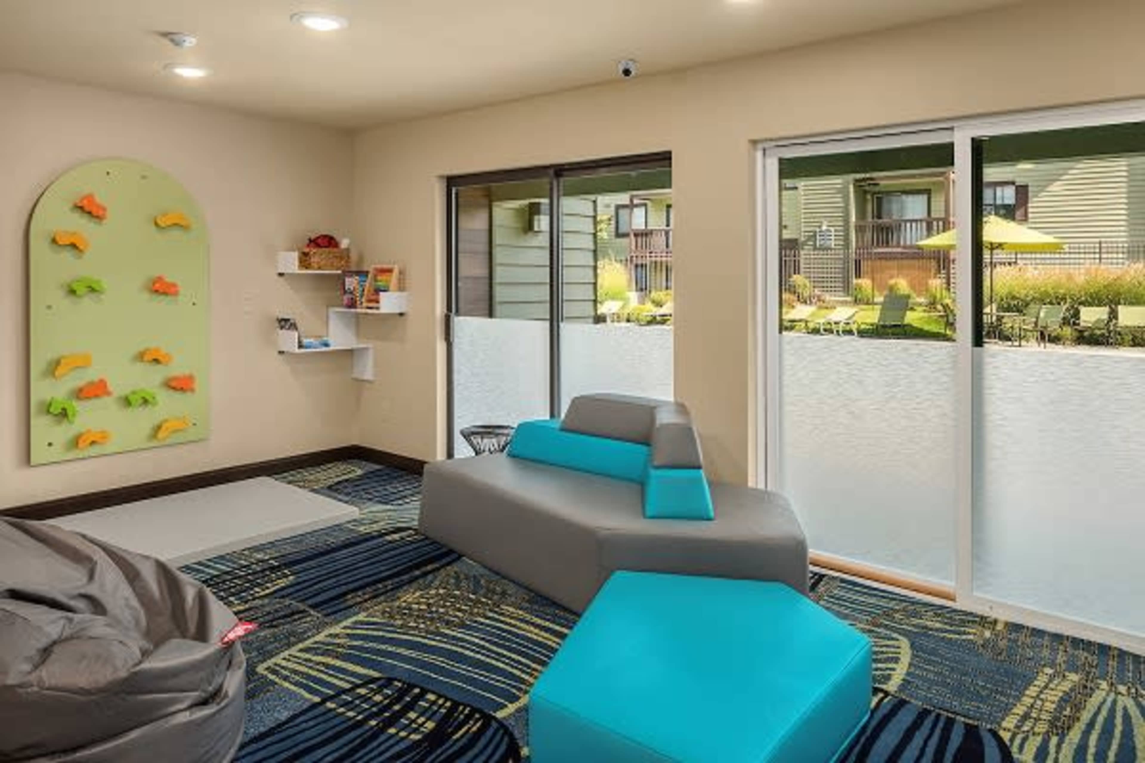 A recreational room with colorful climbing holds on one wall, modern seating, and large windows overlooking a landscaped outdoor area.