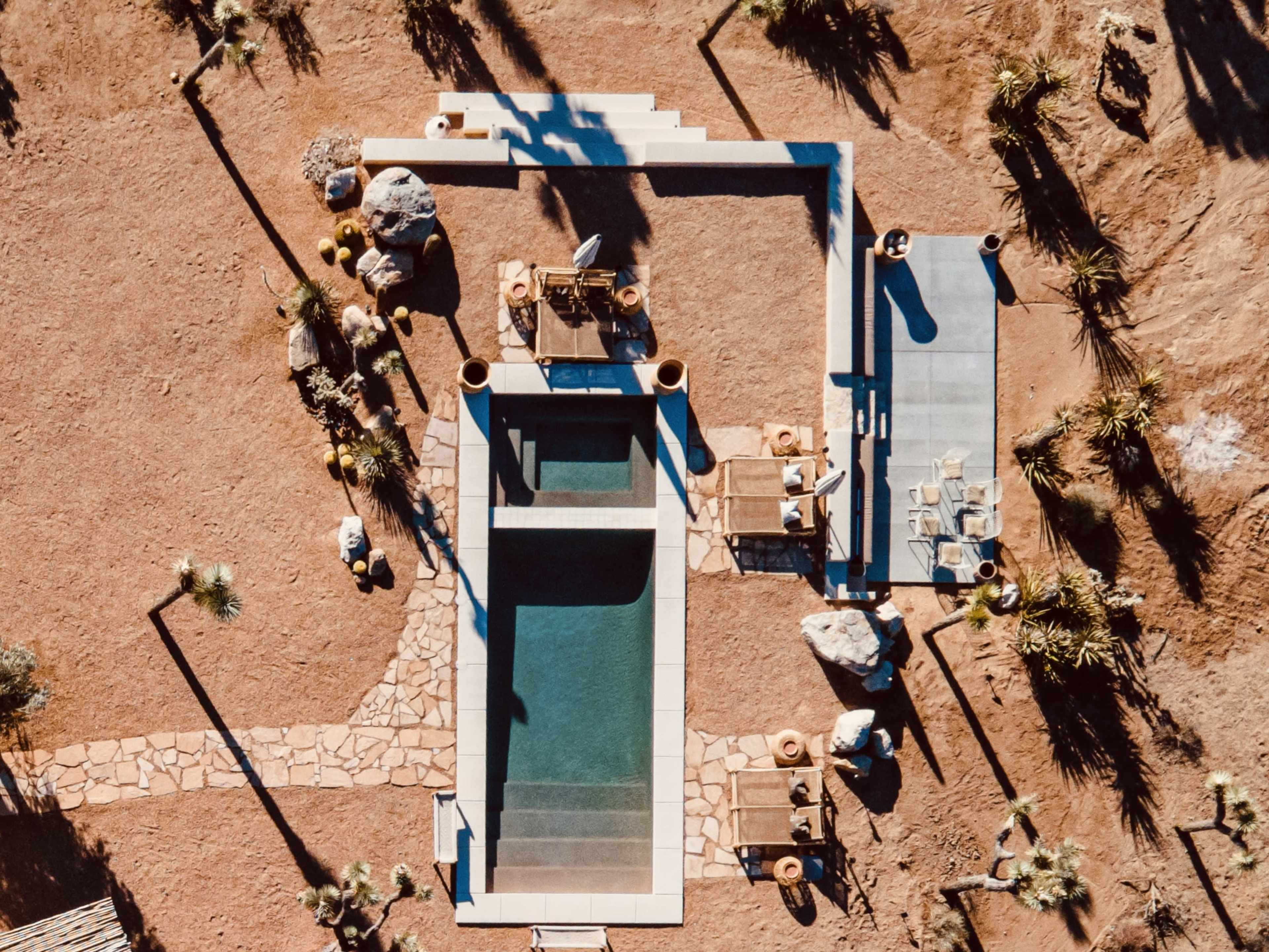An aerial view shows a modern pool surrounded by a stone pathway and desert landscaping.