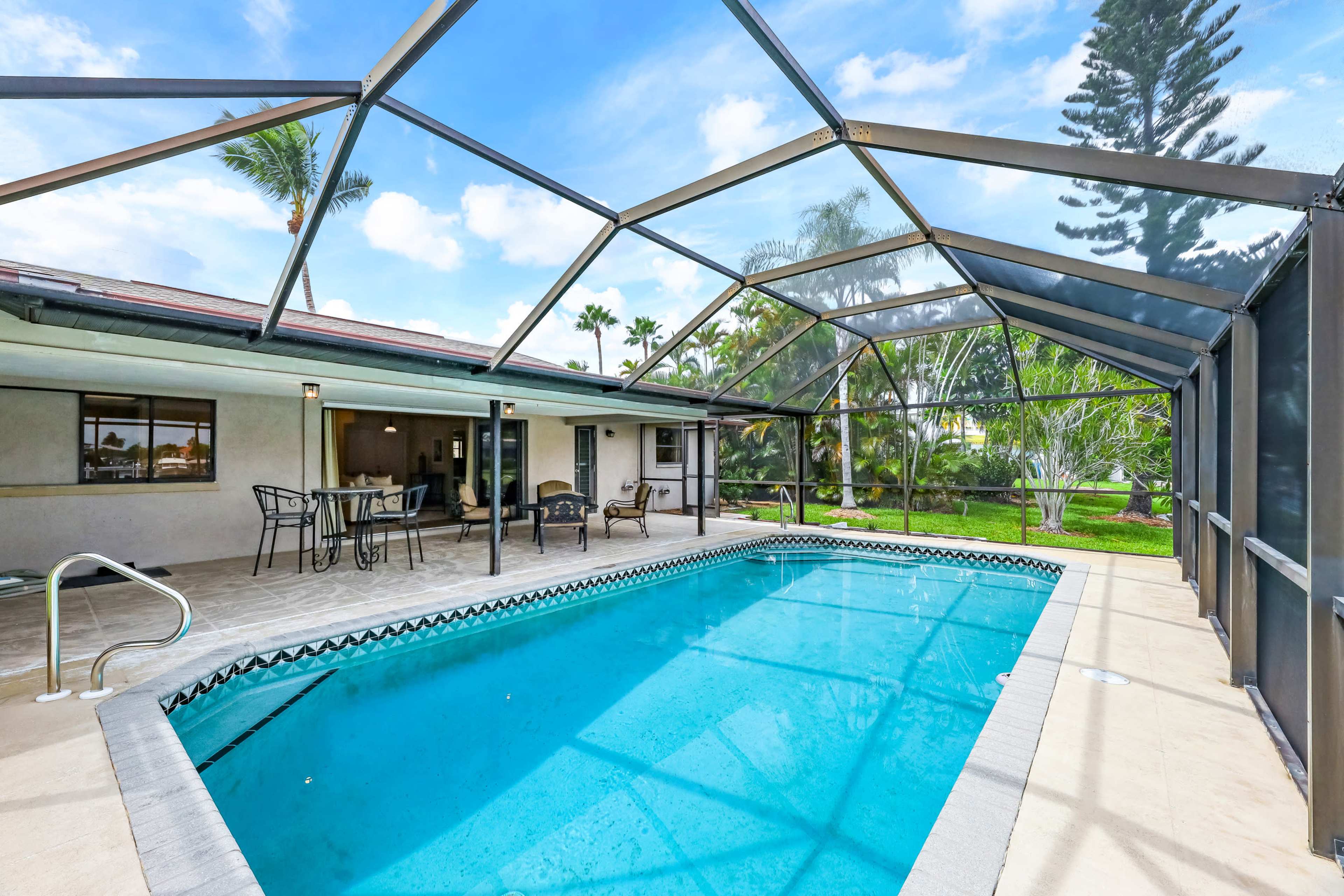 A backyard with a screened-in pool area, featuring a rectangular swimming pool and patio furniture nearby.
