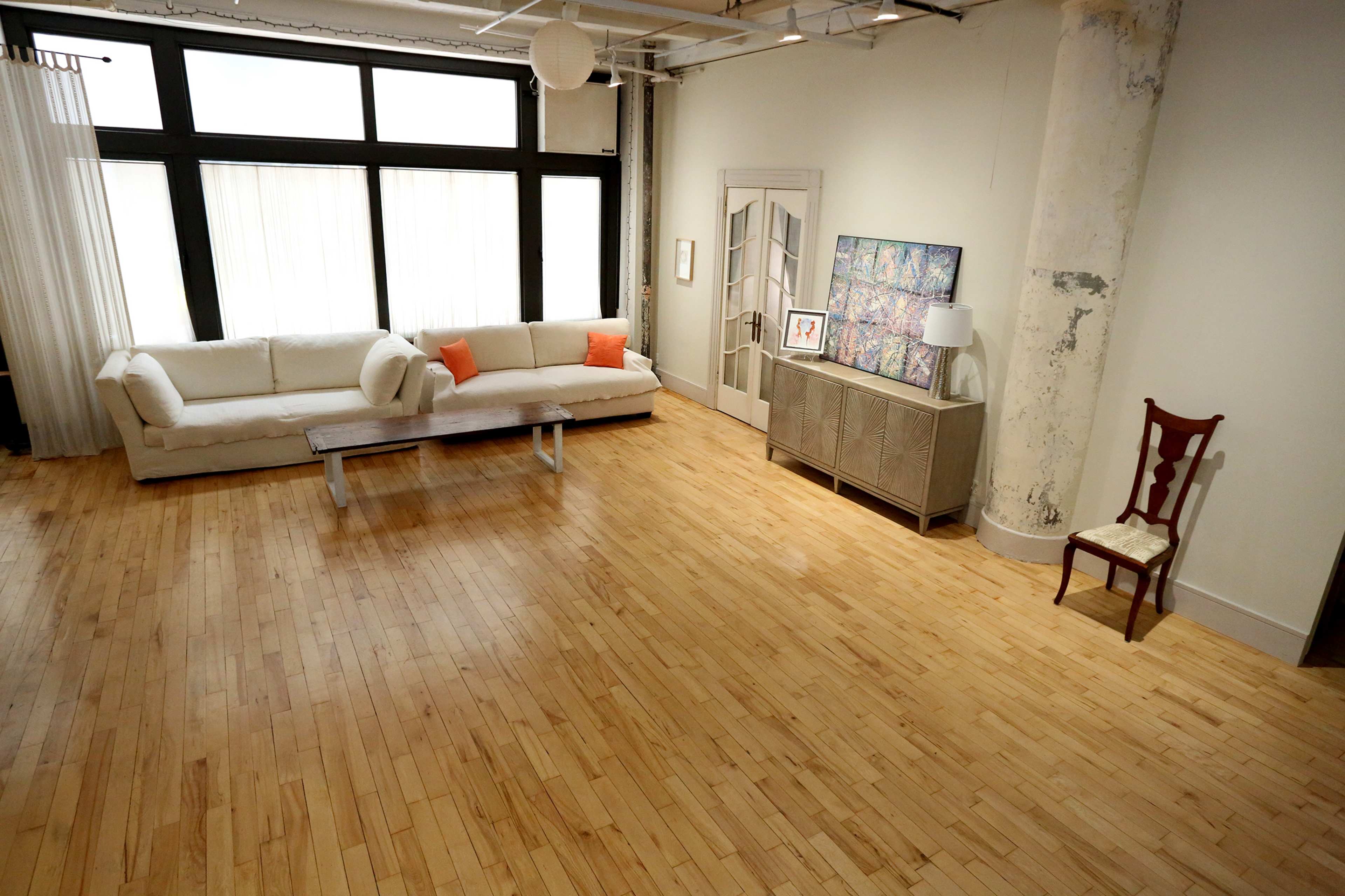 A spacious, modern living room with a light-colored sofa, a wooden coffee table, a cabinet, and a single chair against a wall.