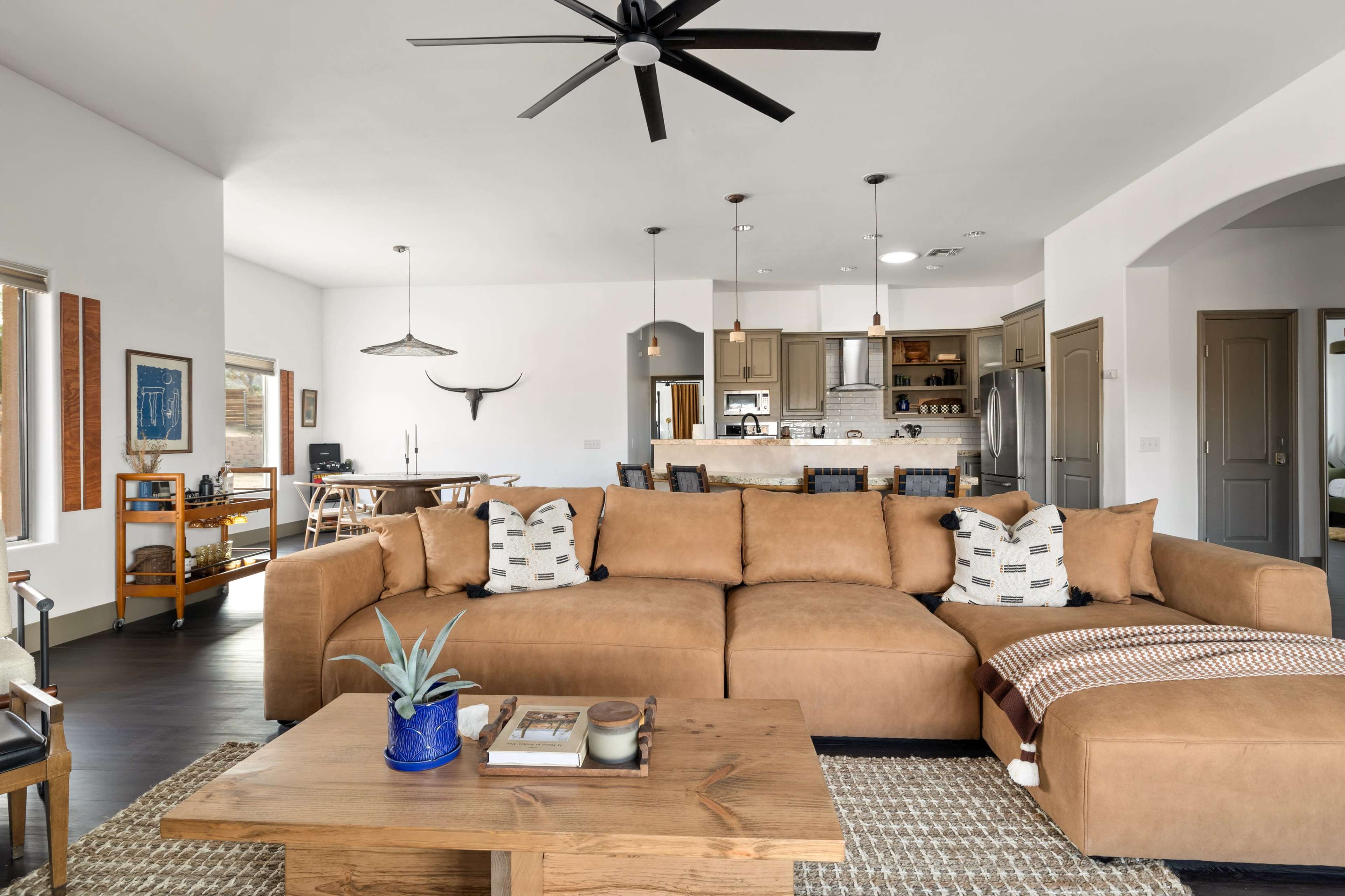 The living room features a large brown sectional sofa, a wooden coffee table, and an open layout connecting to a dining area and kitchen.