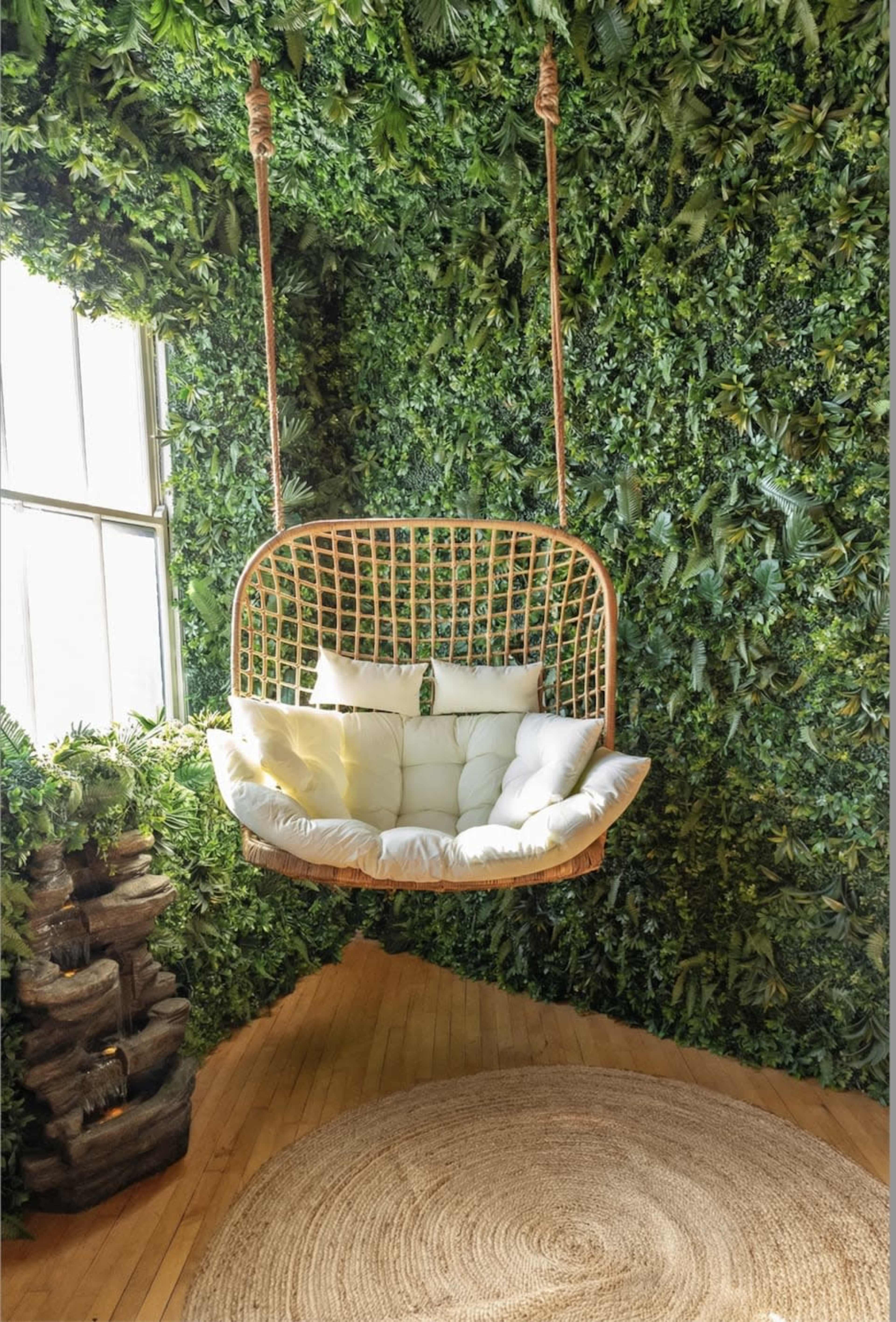 A swing chair with a cushioned seat is suspended in front of a wall covered in lush greenery.