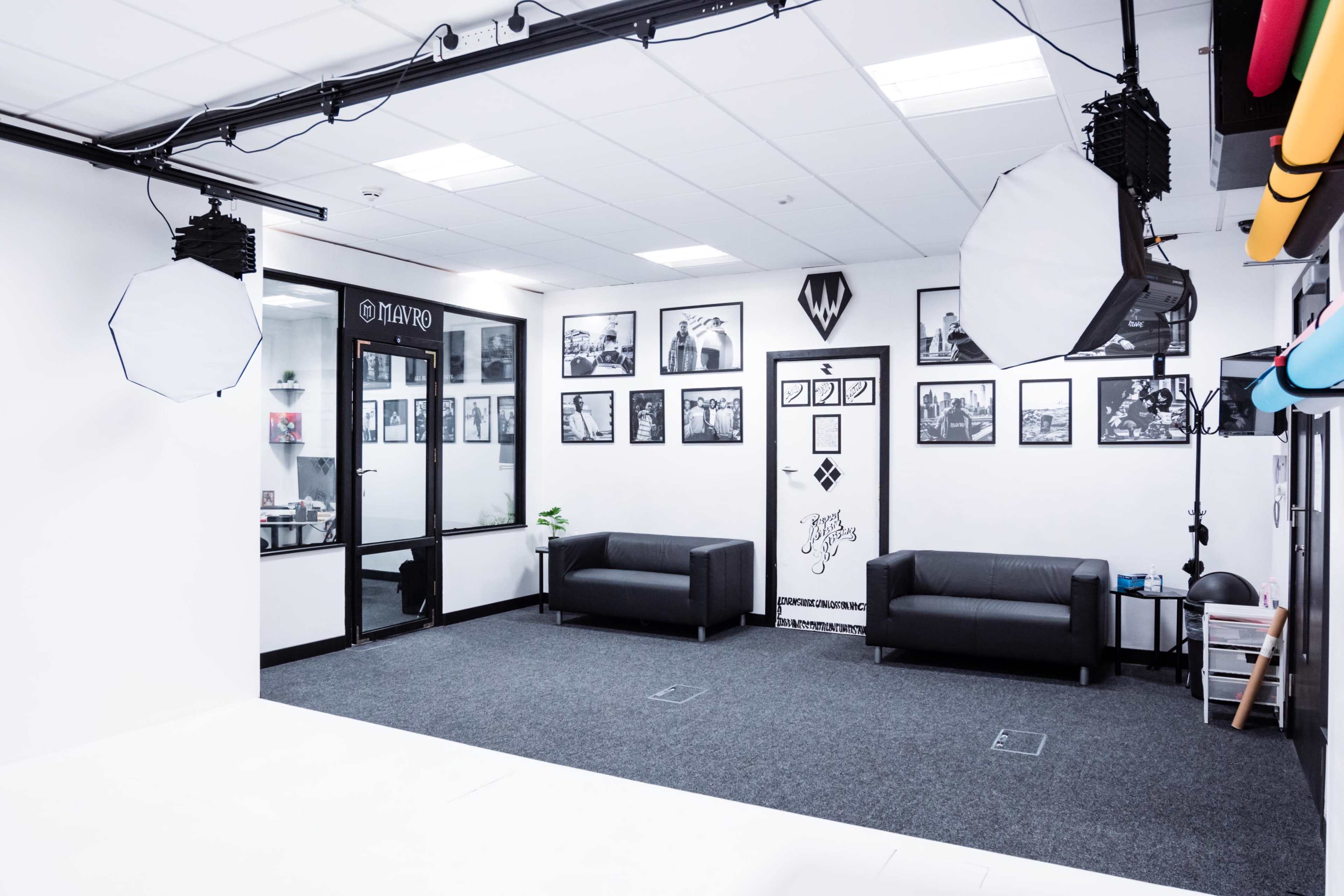 A well-lit photography studio featuring black sofas and framed photographs on the walls.