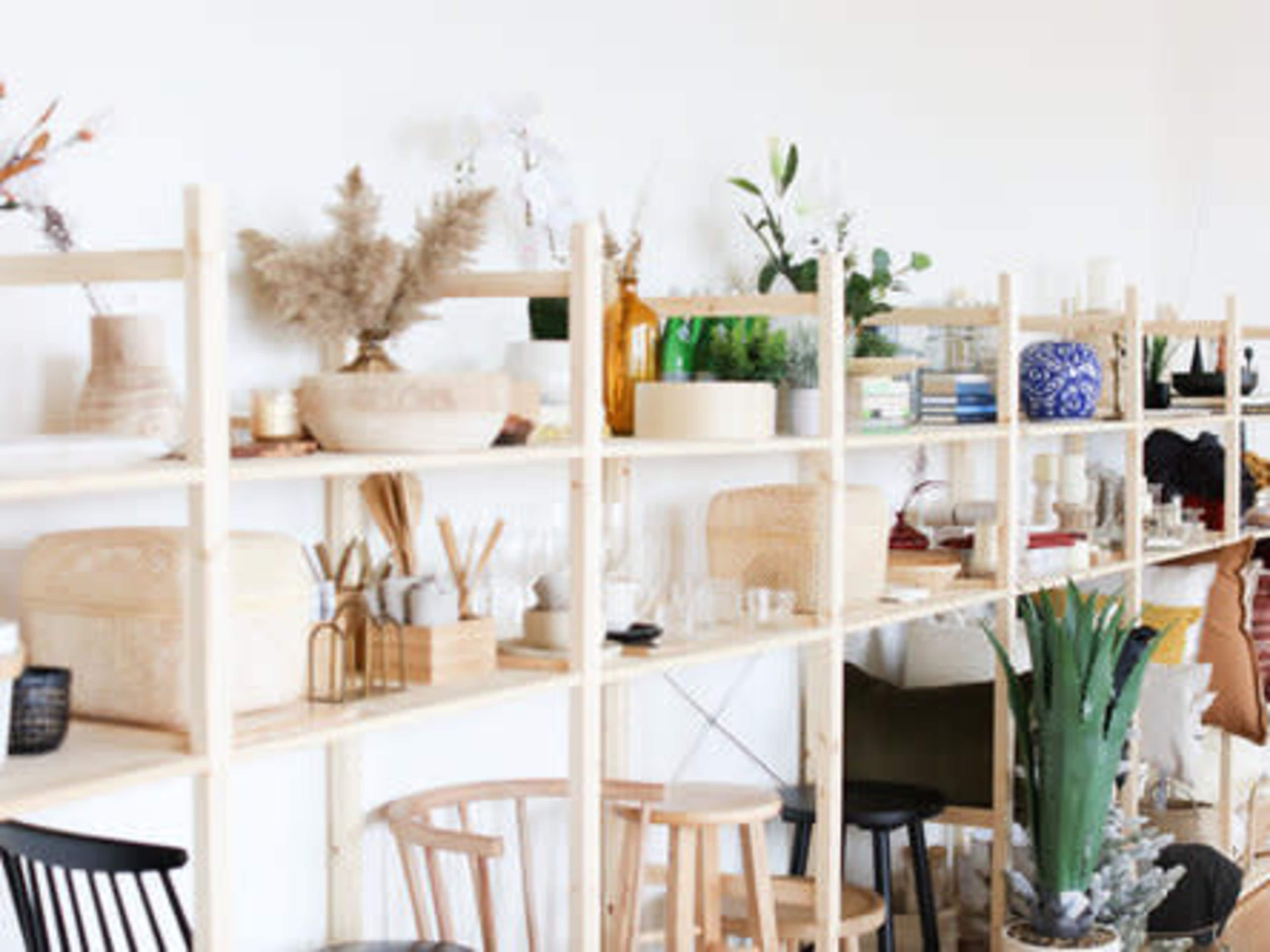 A wooden shelving unit displays a variety of decorative items, plants, and books against a white wall.