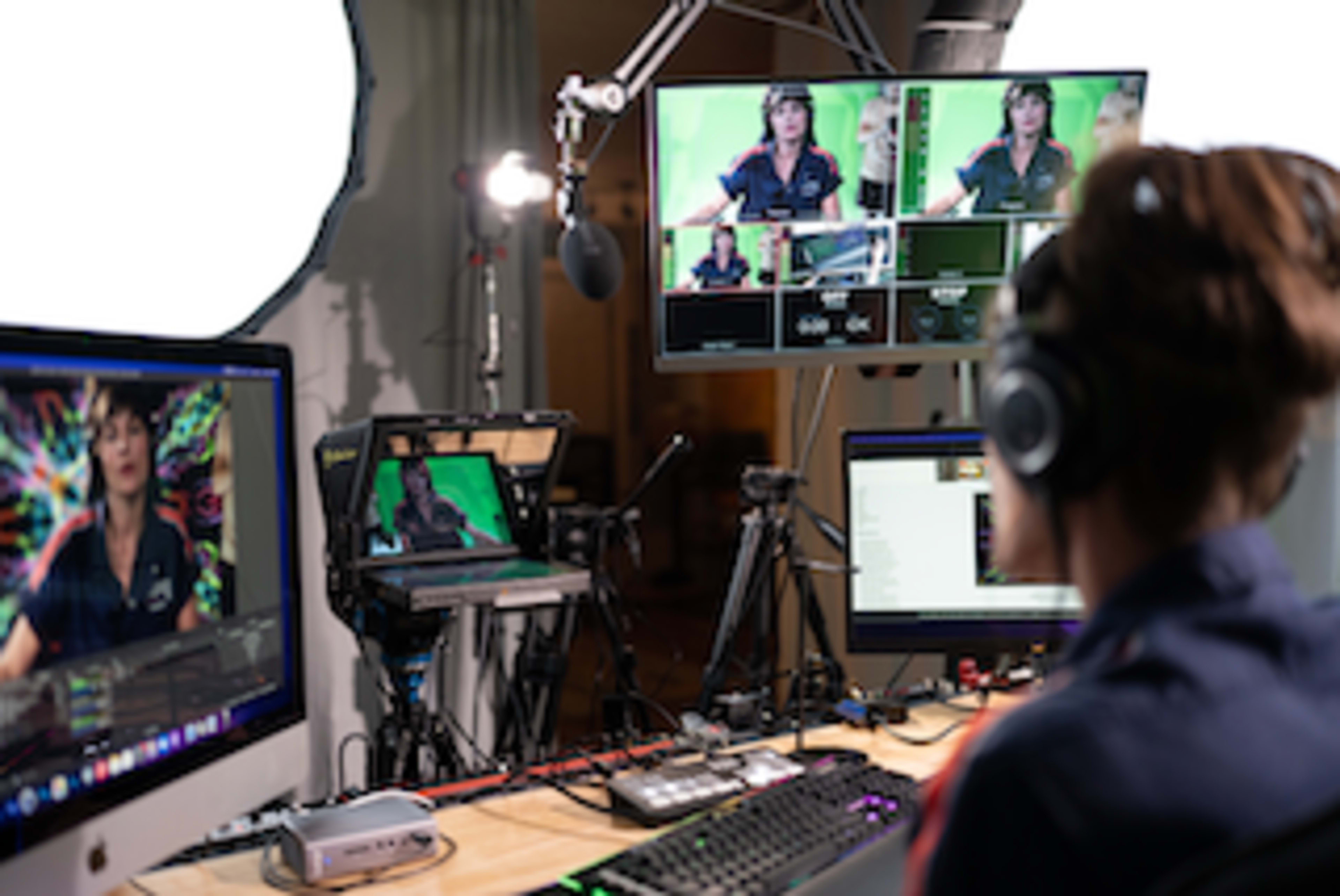 A person with headphones sits at a desk in front of multiple computer monitors displaying a streaming setup with colorful backgrounds.