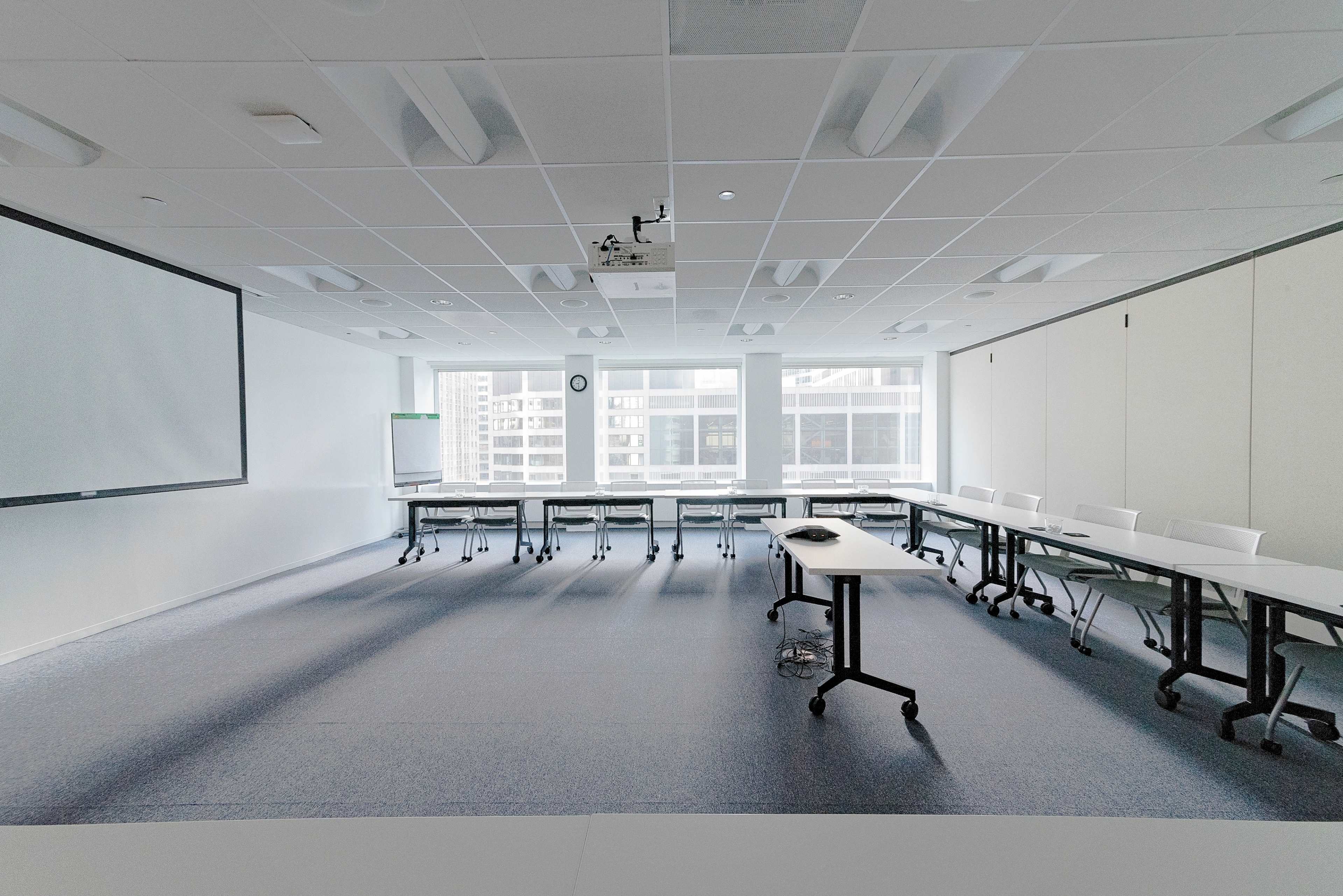 A modern conference room features rows of tables and chairs with large windows providing a view of the city skyline.