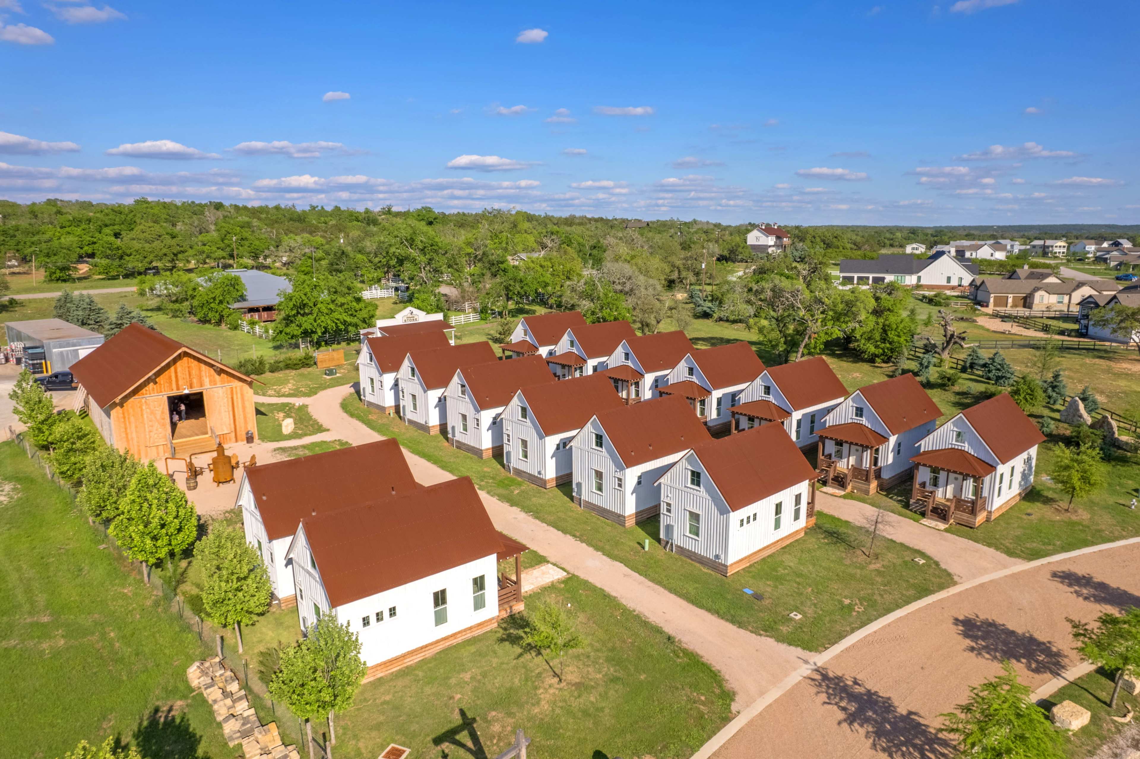 A cluster of small houses with red roofs is arranged around a circular path in a green rural area.