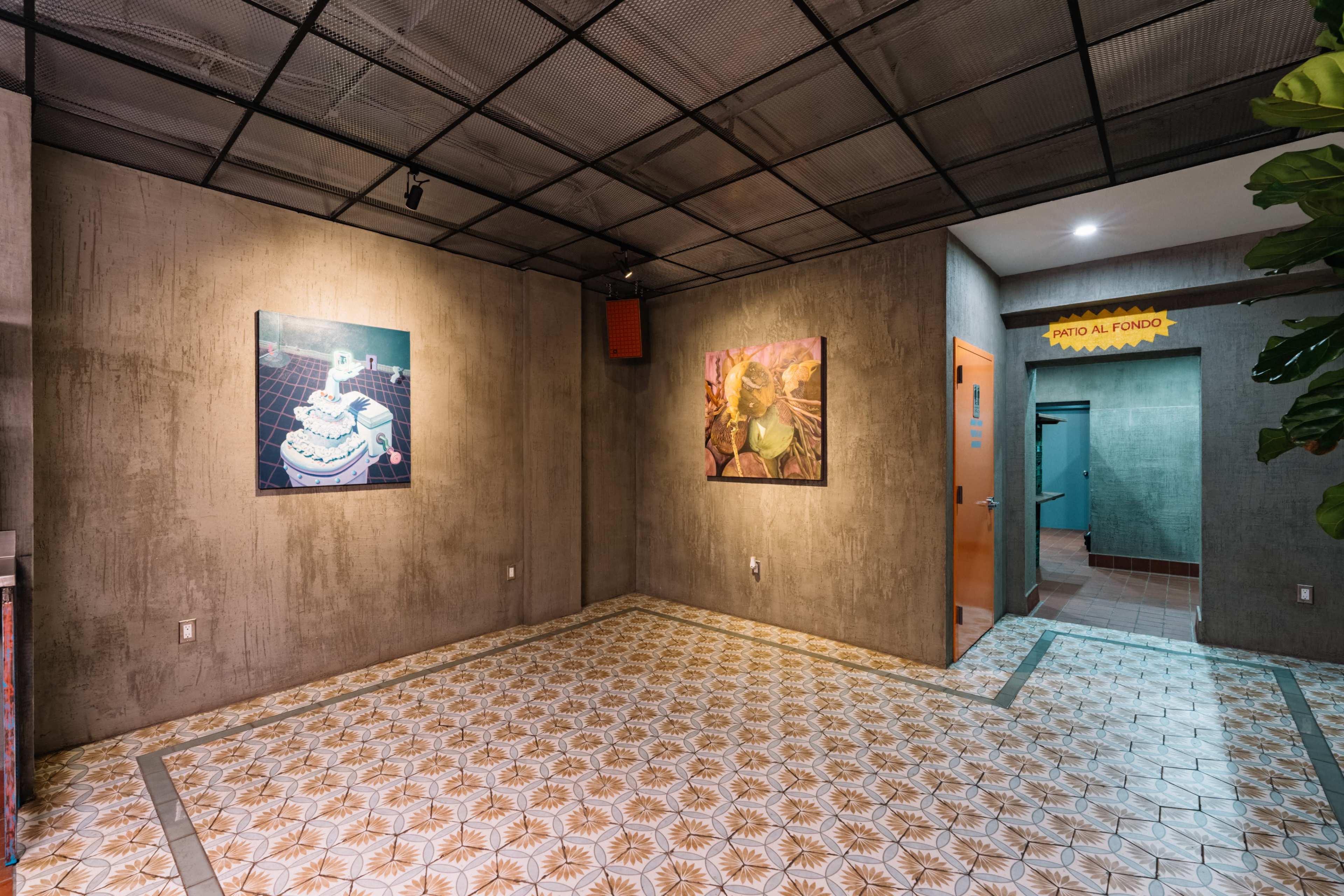The image shows a contemporary interior space with textured gray walls, two framed artworks hanging, and a decorative tiled floor, leading to a doorway marked with a sign.
