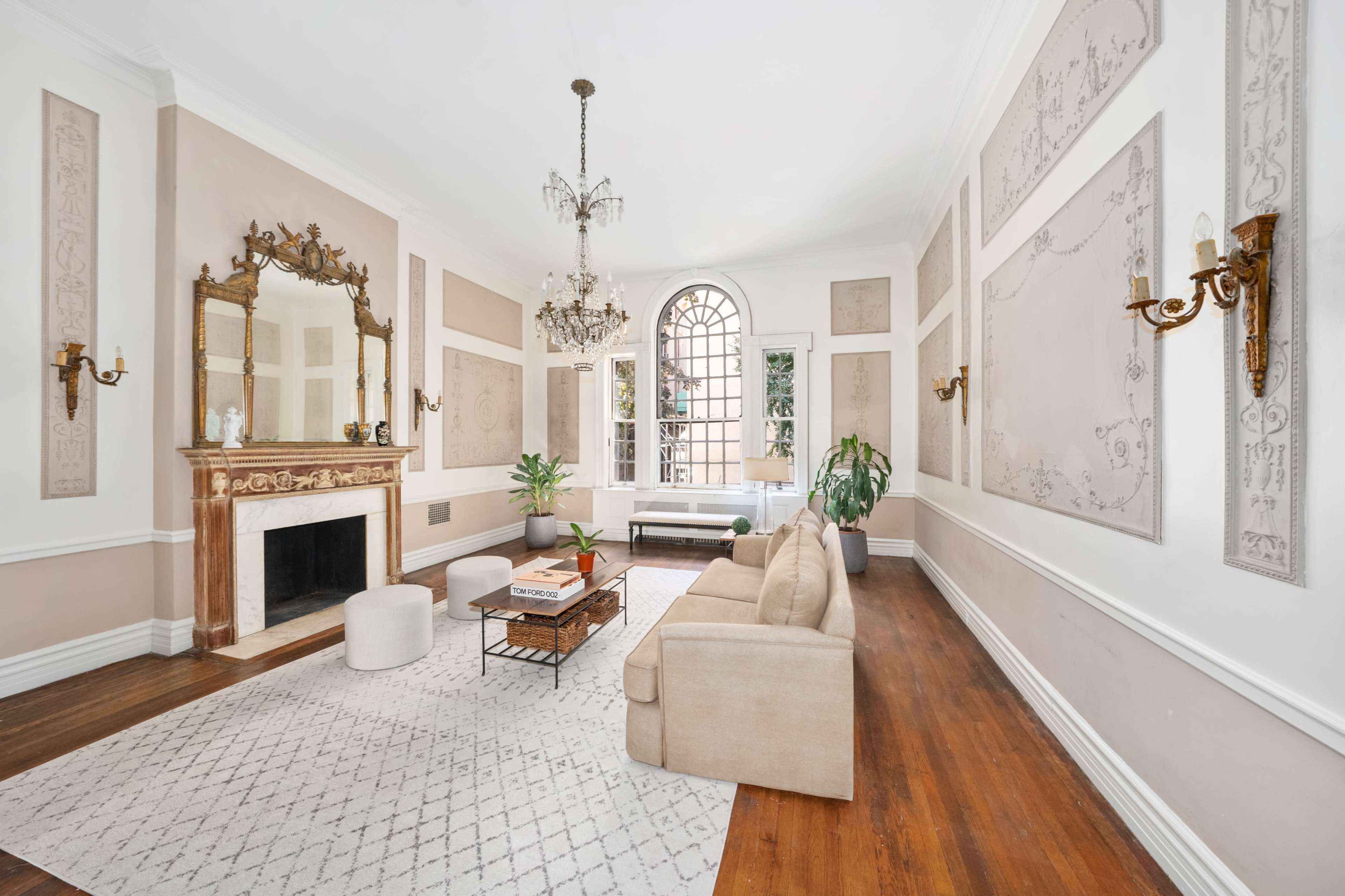 A spacious living room with a beige sofa, a coffee table on a light-colored rug, a fireplace, and large windows allowing natural light to enter.