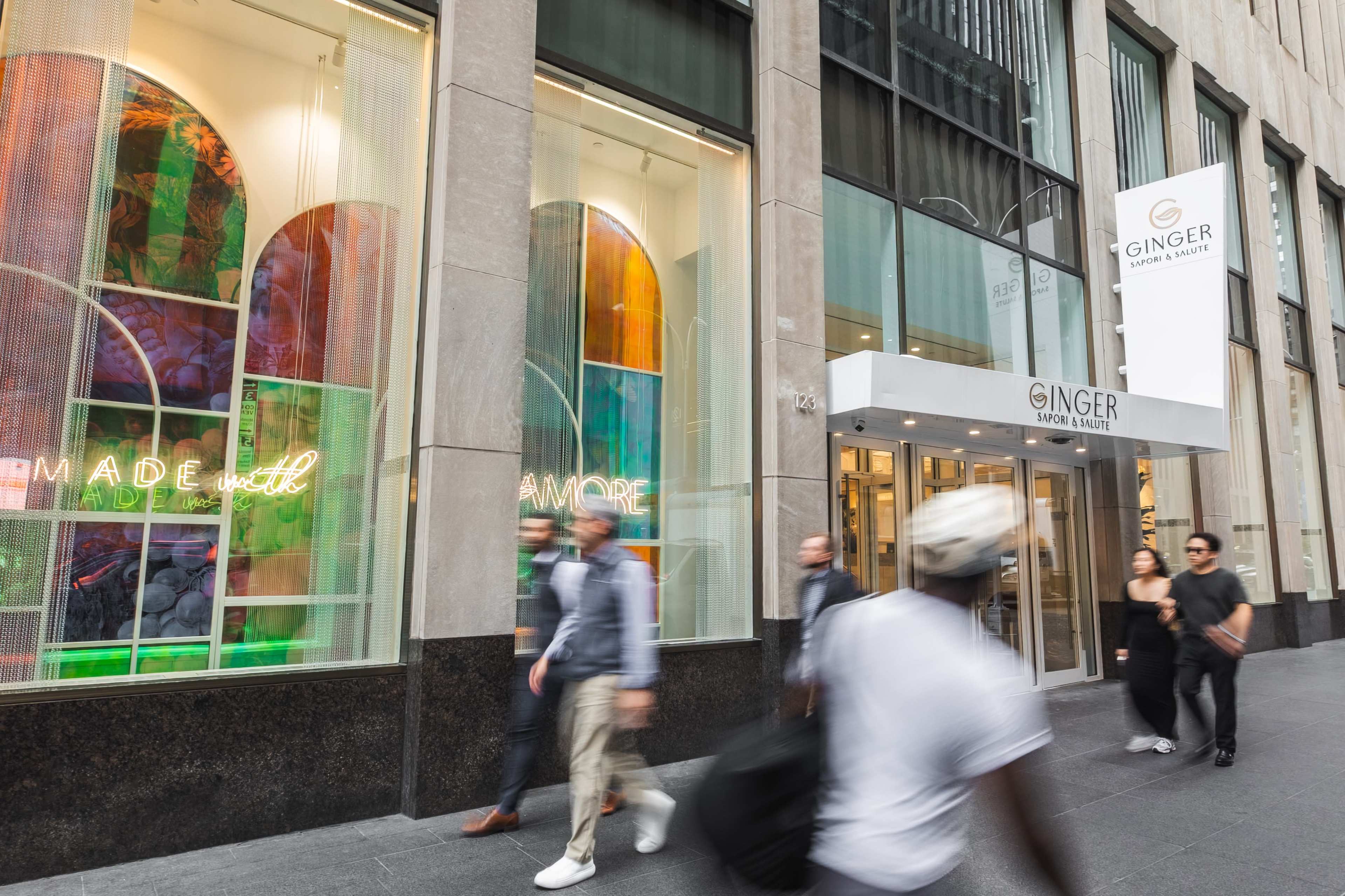 The image shows a modern storefront named "GINGER" with colorful stained glass windows and people walking past on a city street.