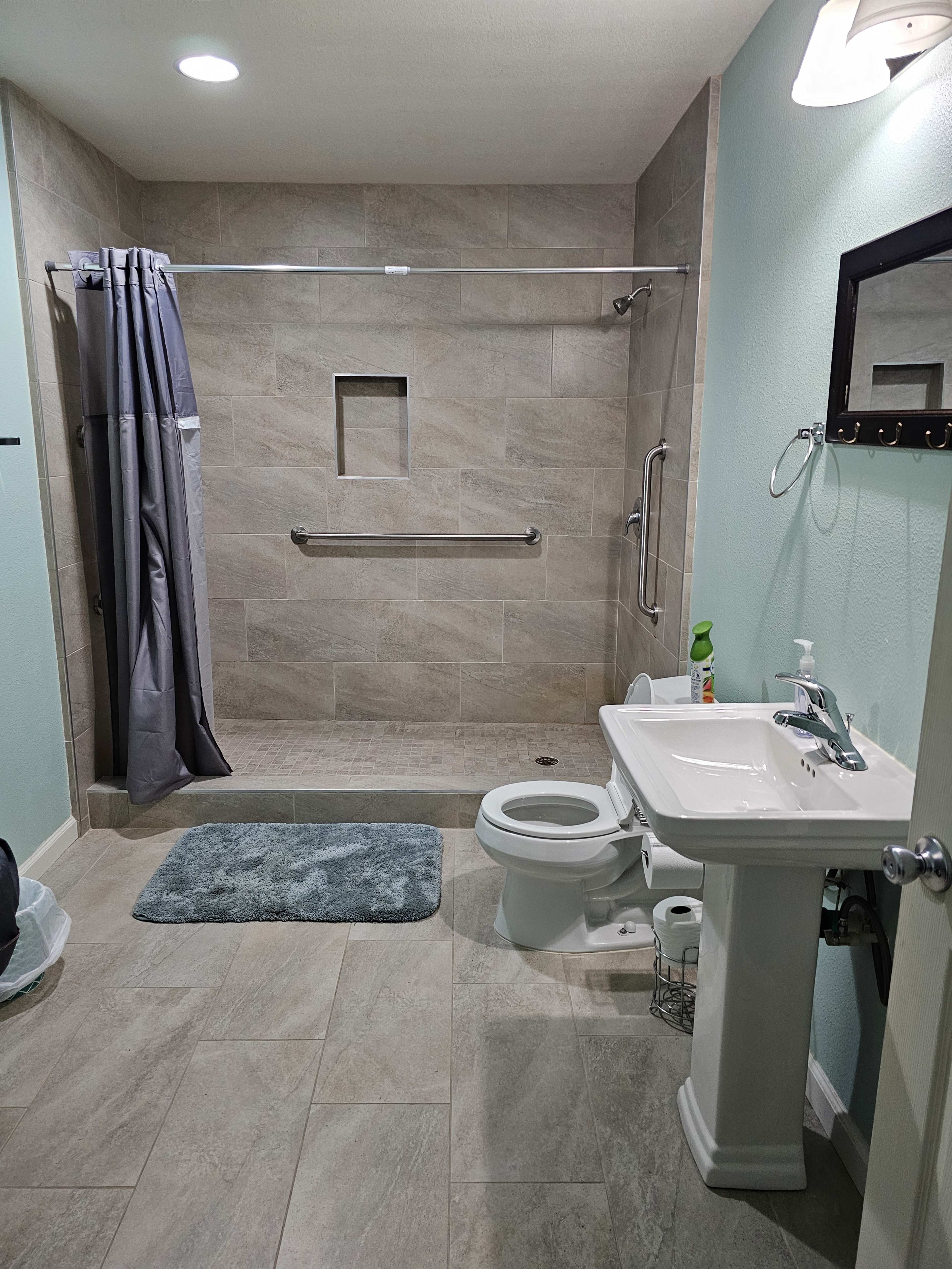 A modern bathroom featuring a walk-in shower with a glass door, a white pedestal sink, a toilet, and light-colored tiled flooring.