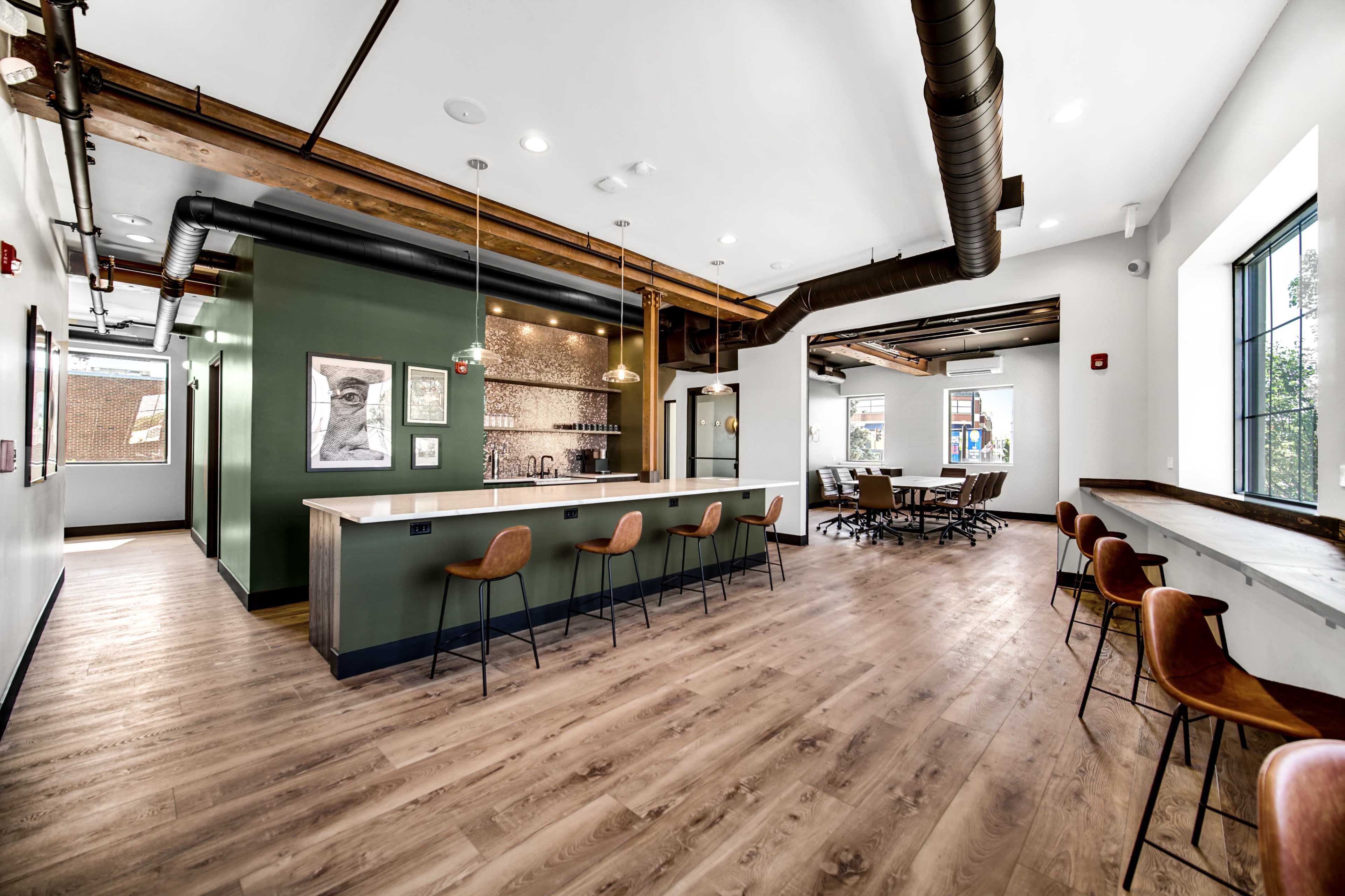 A modern office space with a bar area and a conference room featuring wooden flooring and industrial design elements.
