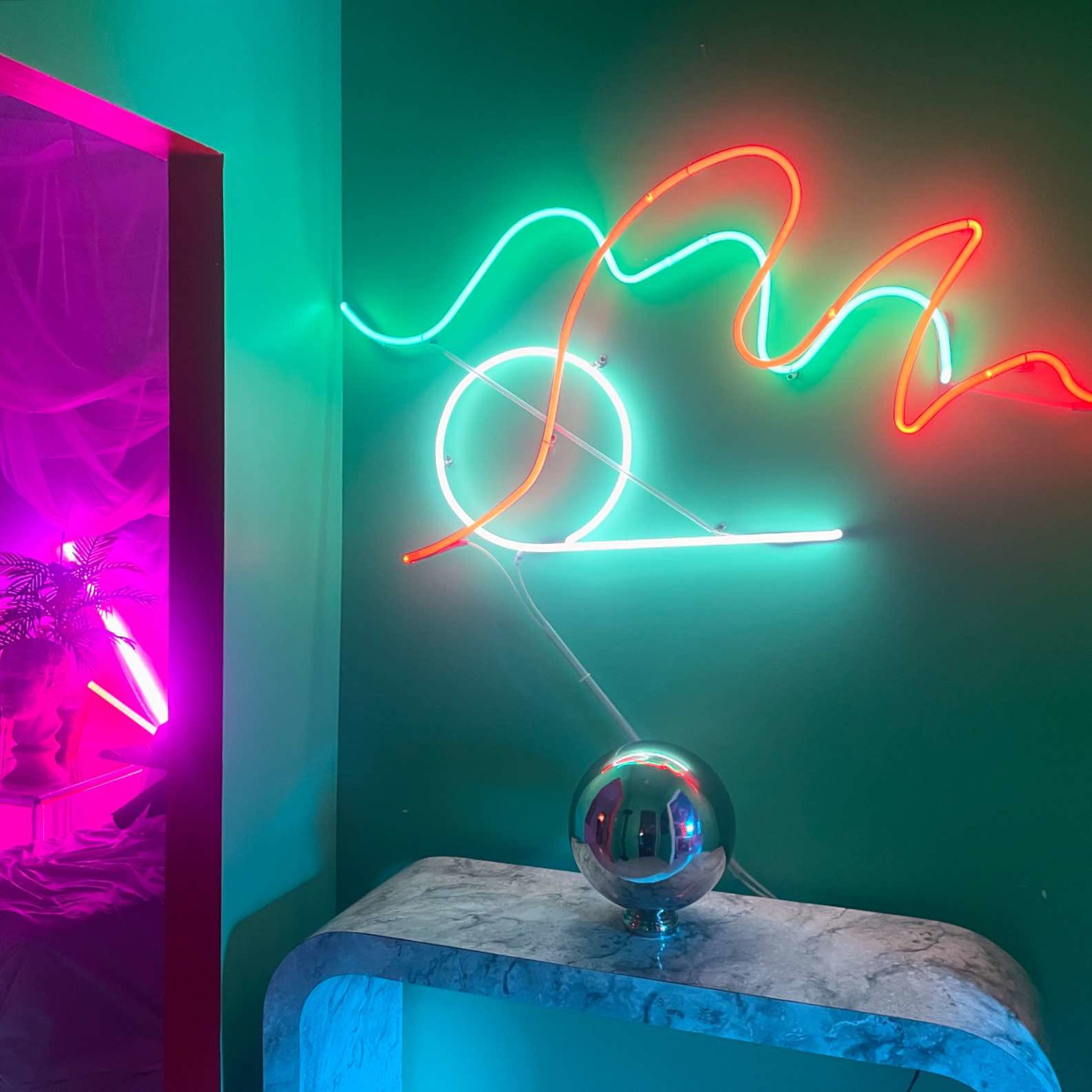 The image features a modern interior with colorful neon lights against a green wall, and a shiny sphere on a marble surface.