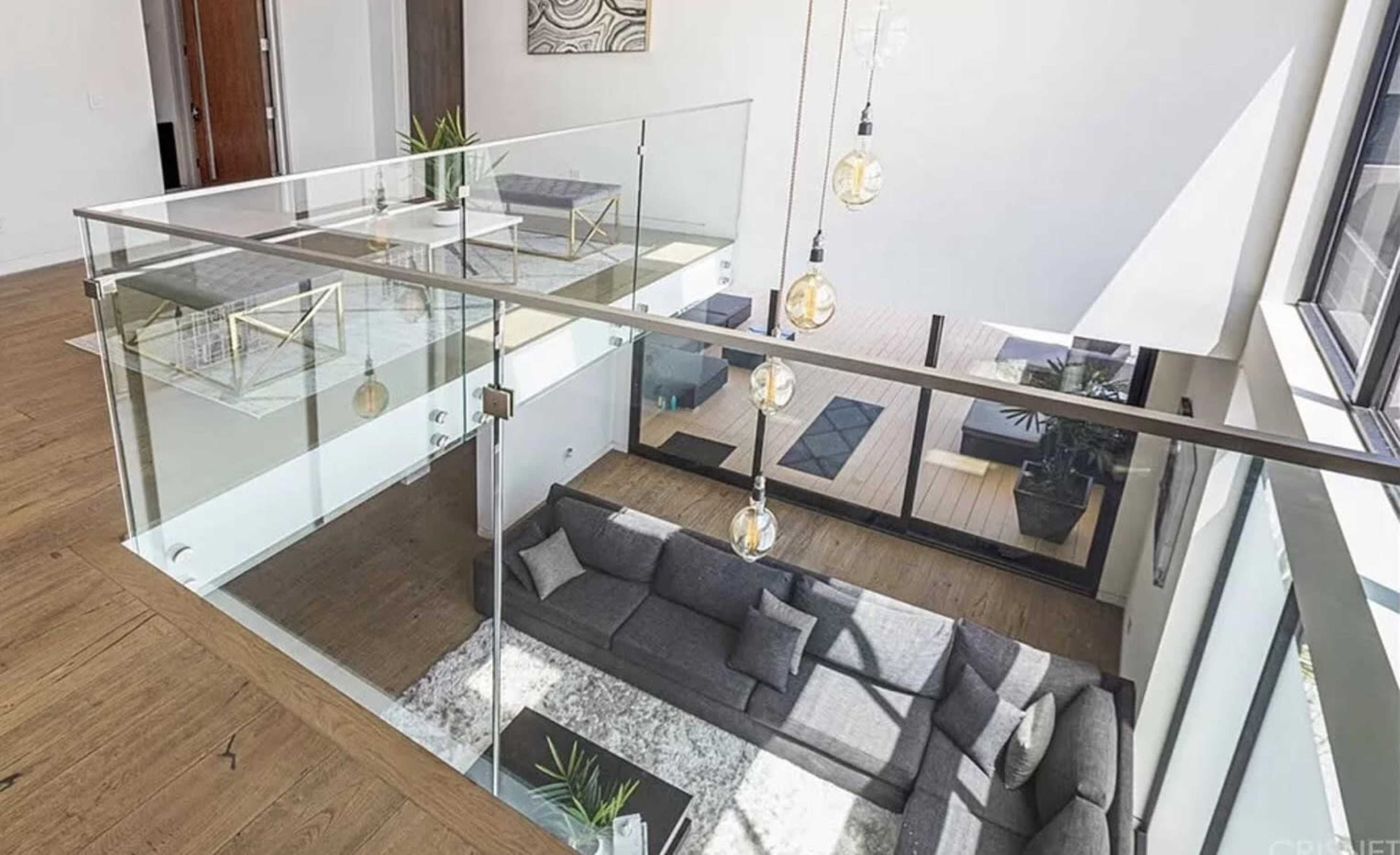A modern living space features a sectional sofa and a balcony with glass railings overlooking an open floor plan.
