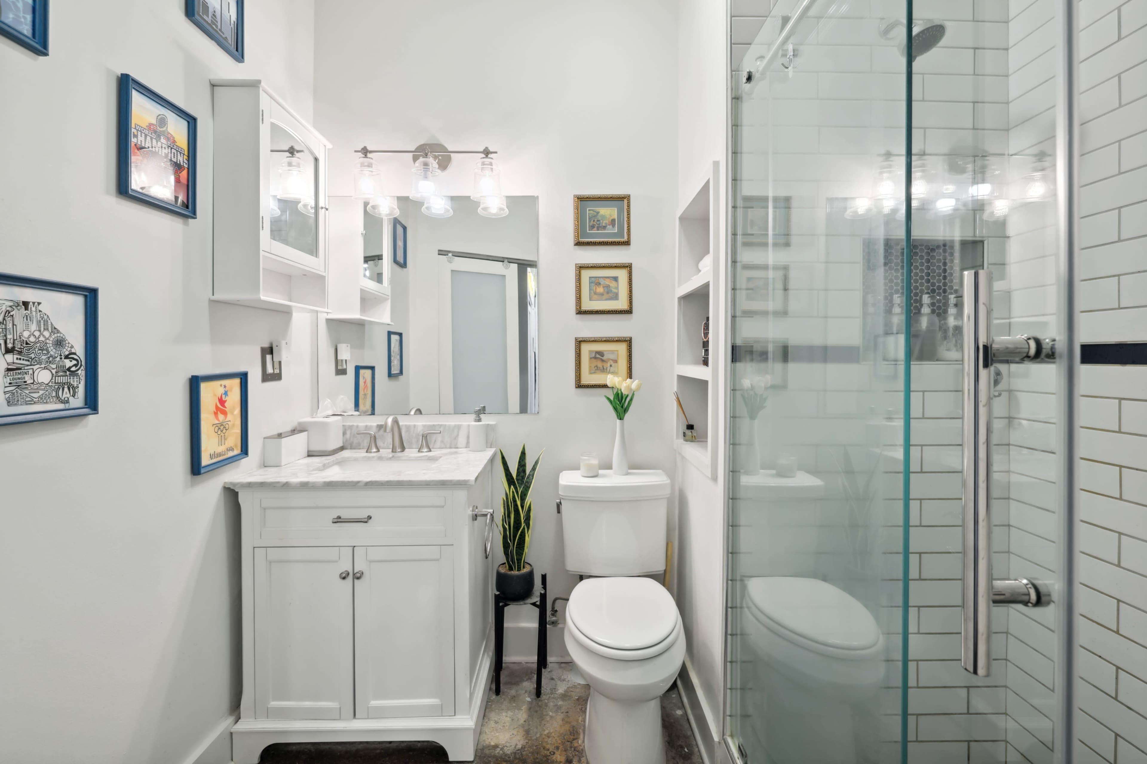 A modern bathroom featuring a white vanity with a marble countertop, a glass-enclosed shower, and framed artwork on the walls.