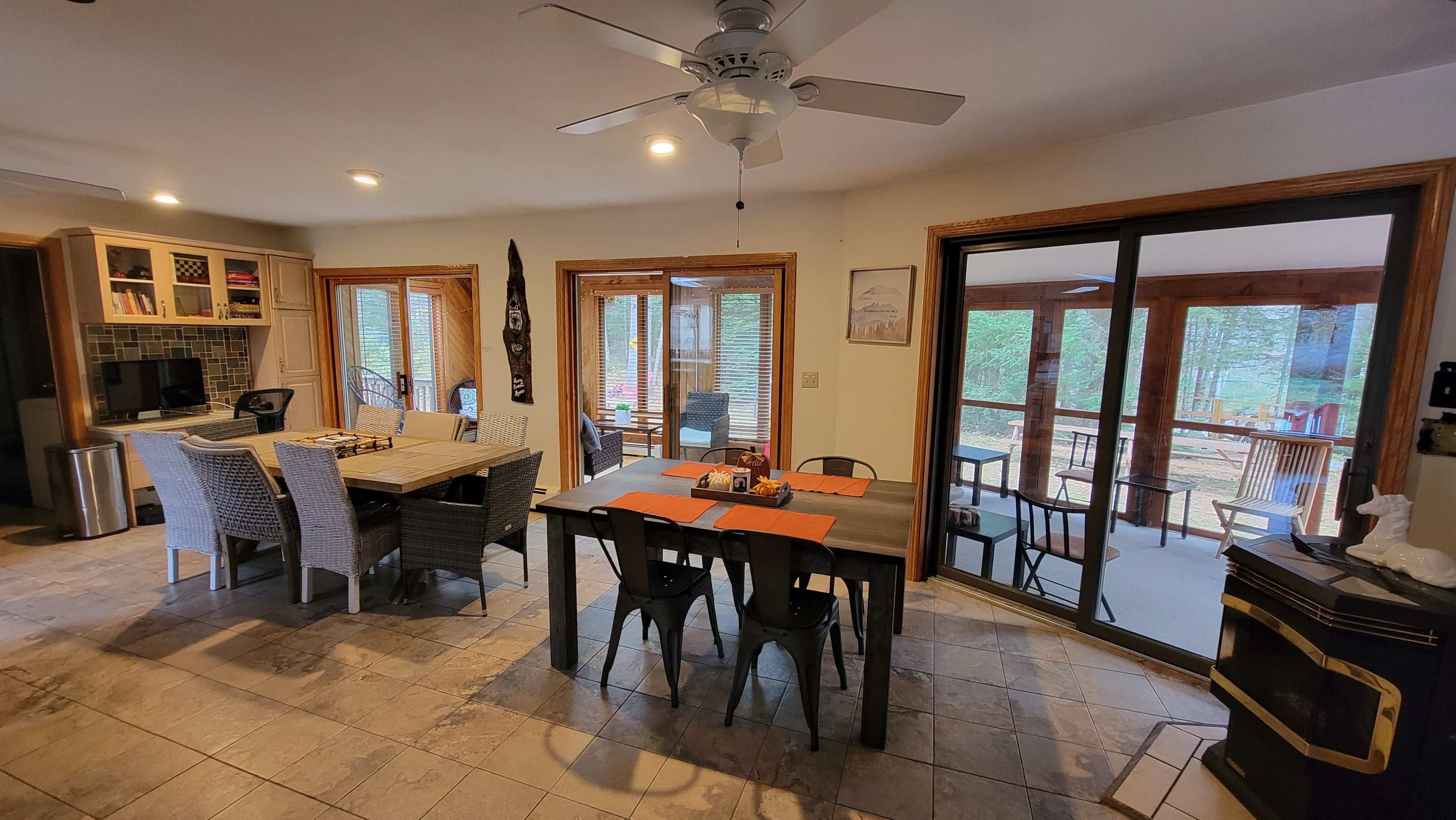 A spacious dining area with a large table set for a meal, surrounded by windows that provide a view of an outdoor porch.
