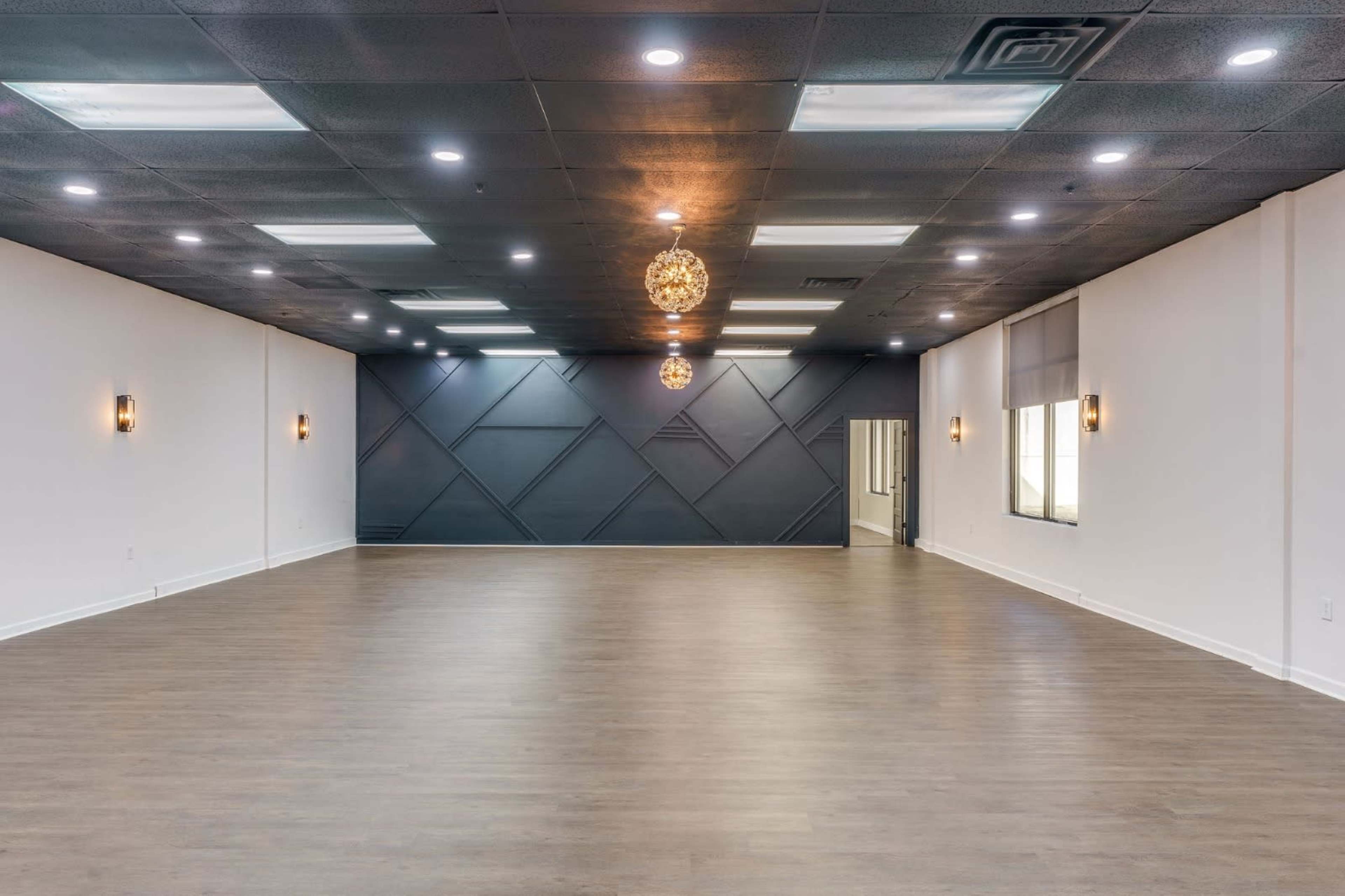 The image shows a spacious, empty interior room with wooden flooring and dimmed overhead lighting.