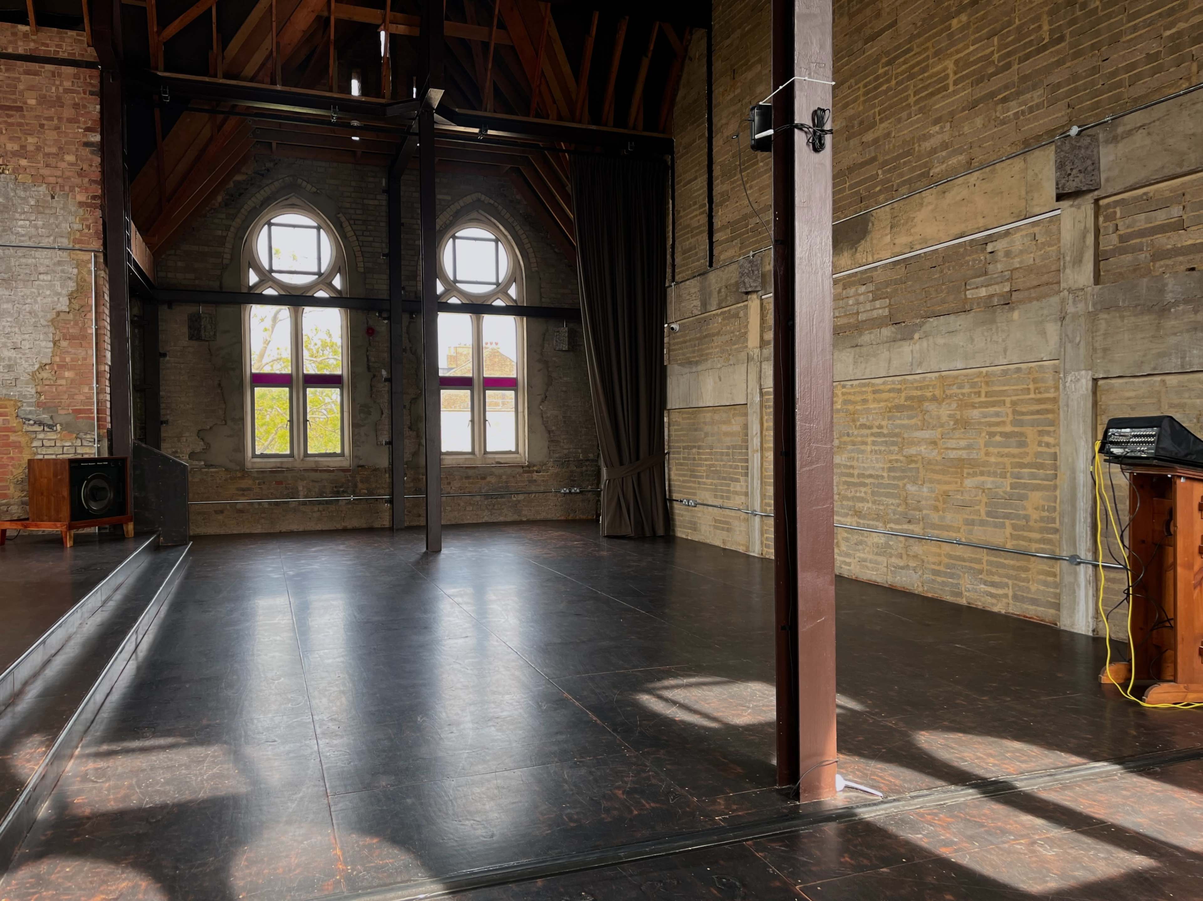 The image shows an empty dance studio with wooden beams and large arched windows allowing natural light to enter.