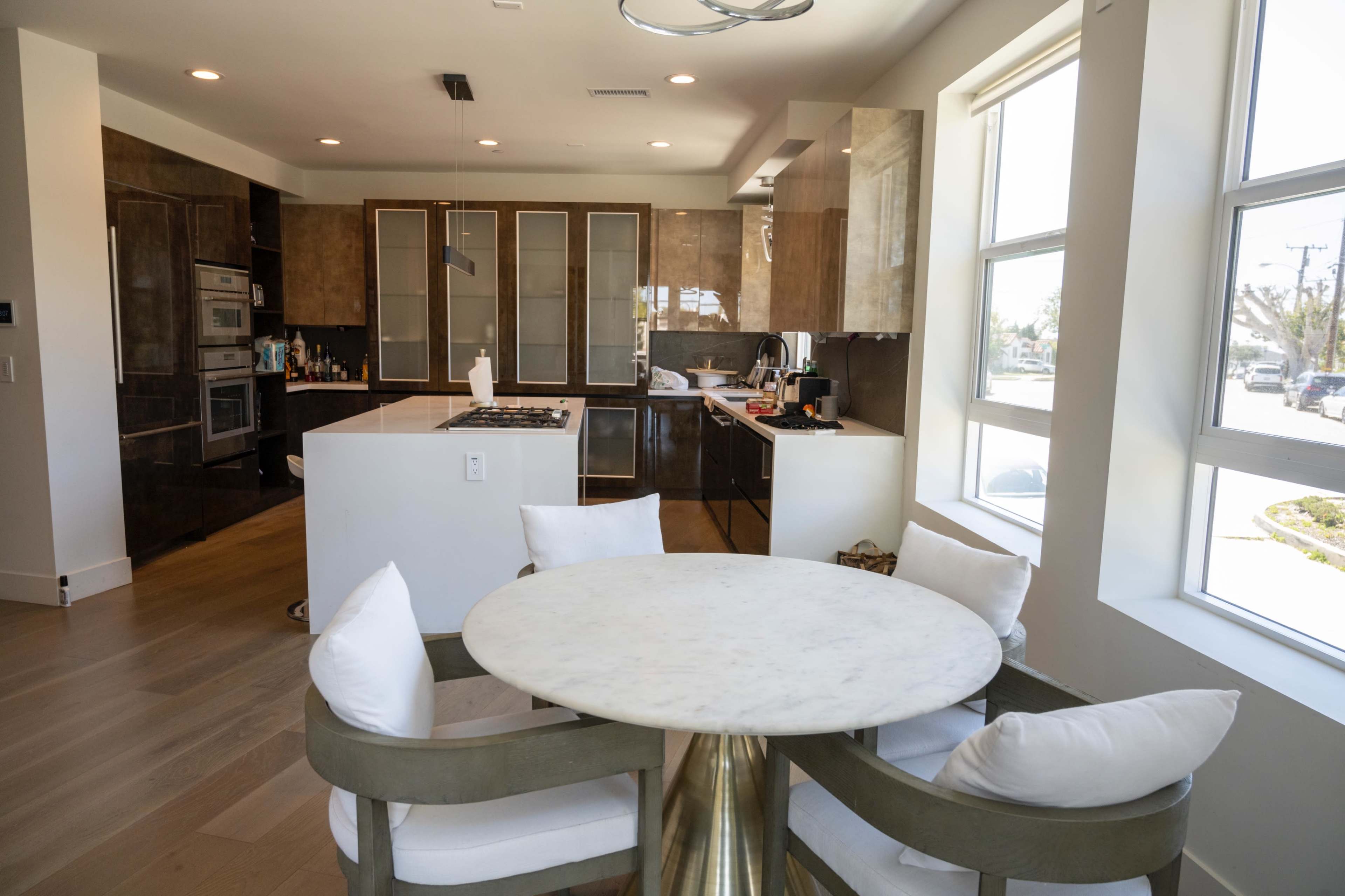 A modern kitchen features dark cabinetry, a central island with a stovetop, and a round dining table with white cushions.