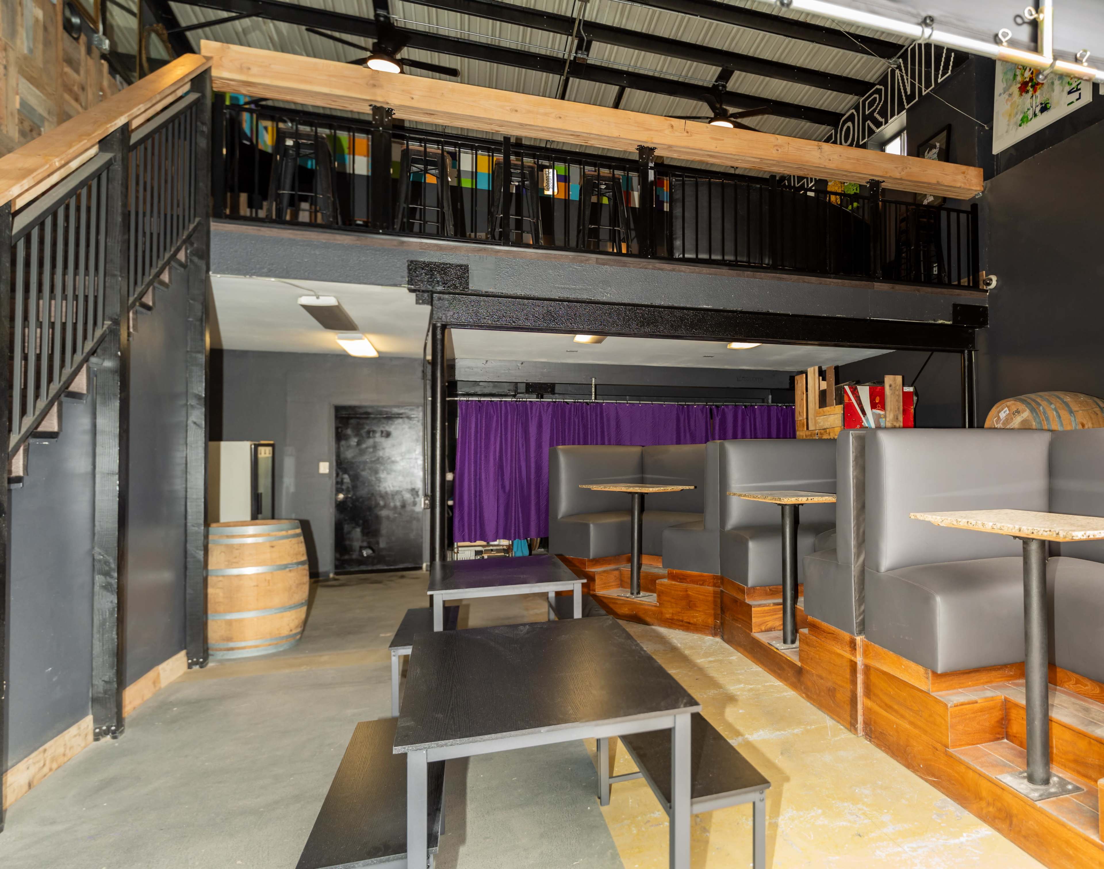 A modern indoor space featuring a two-level seating area with wooden accents, black furniture, and a purple curtain in the background.