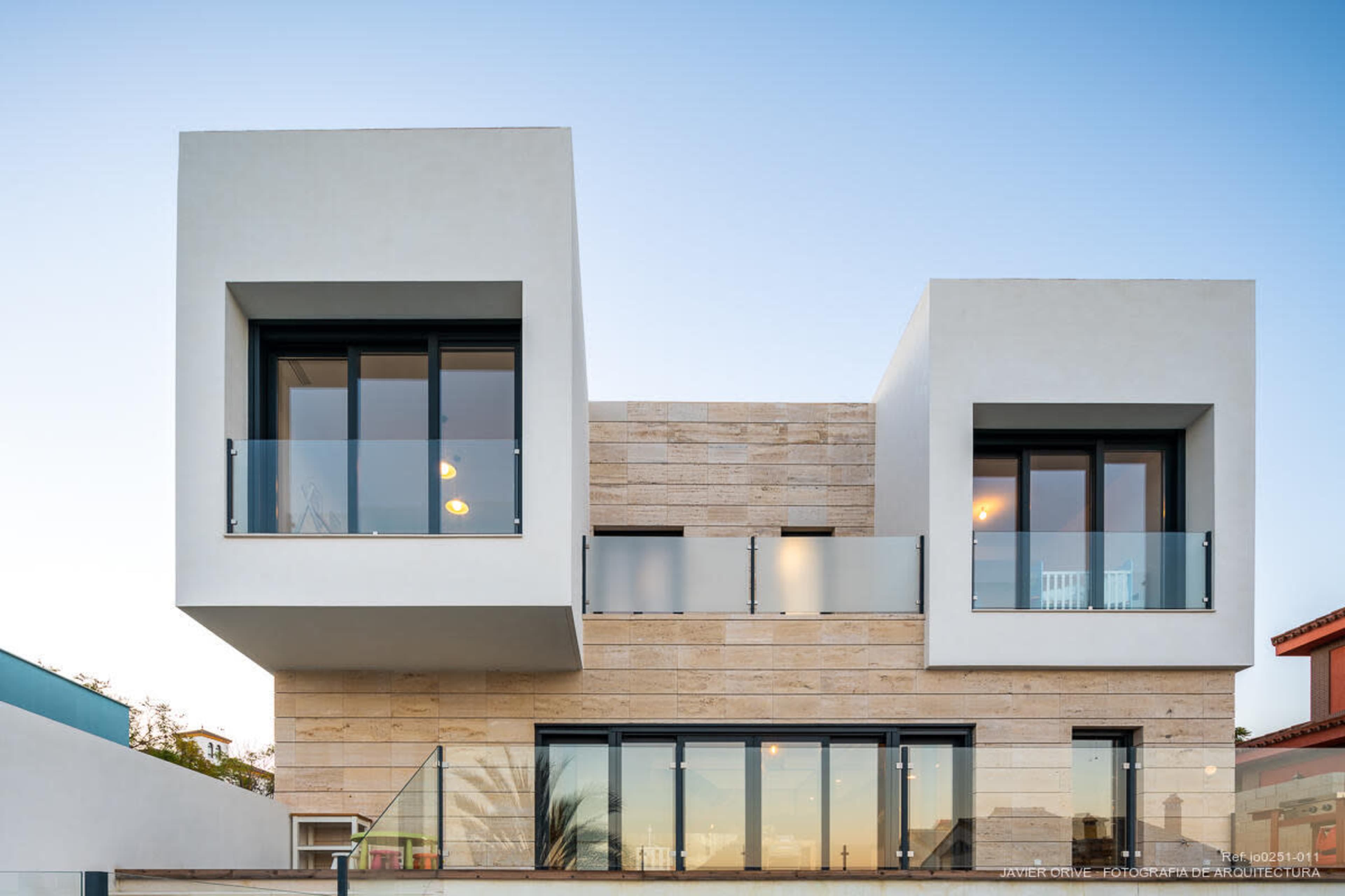 The image shows a modern two-story house with a combination of rectangular shapes, large windows, and a balcony.