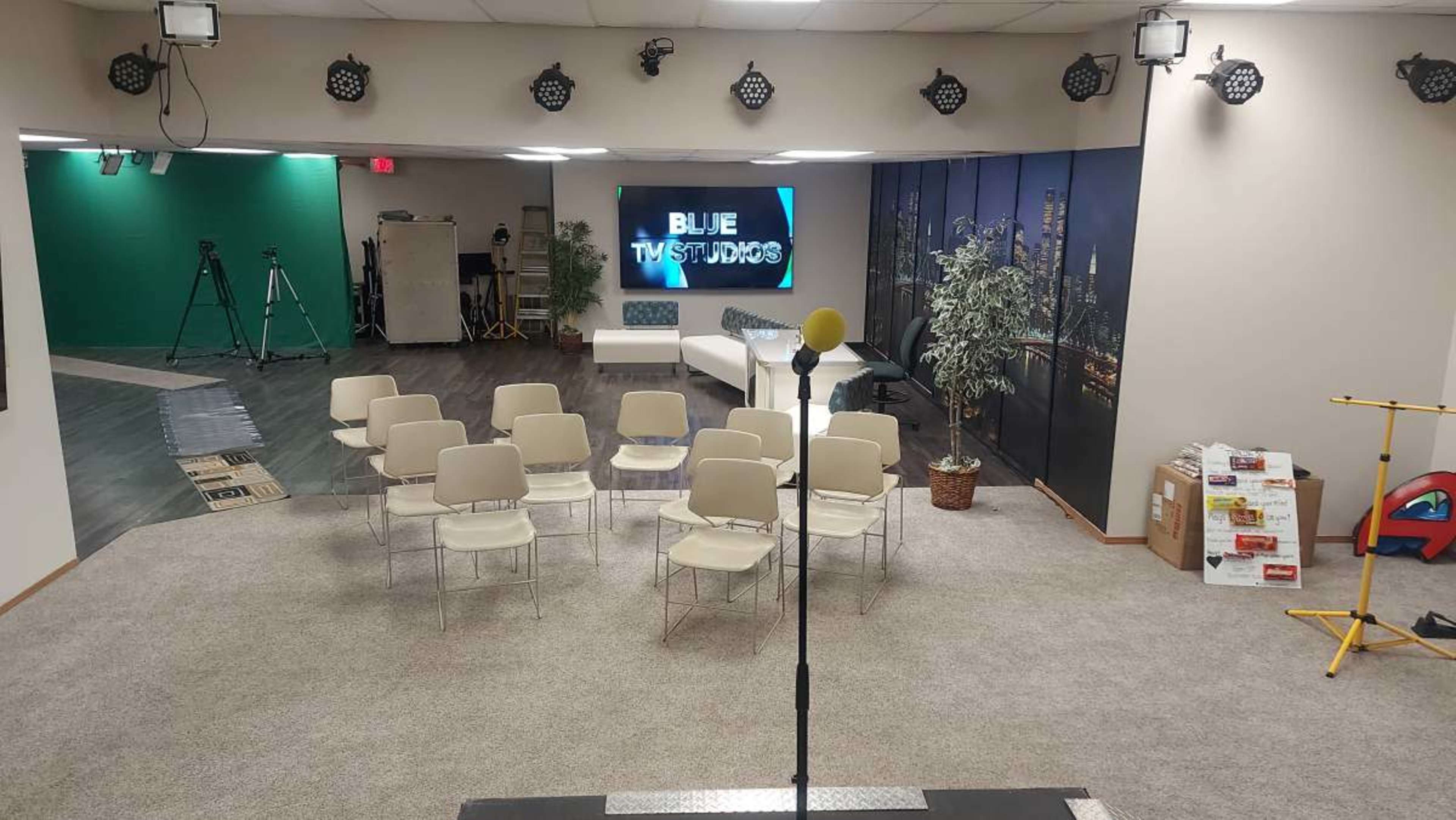 A studio setup with rows of chairs facing a microphone stand and a display screen that reads "BLUE TWIST STUDIOS," with green and black backdrops in the background.